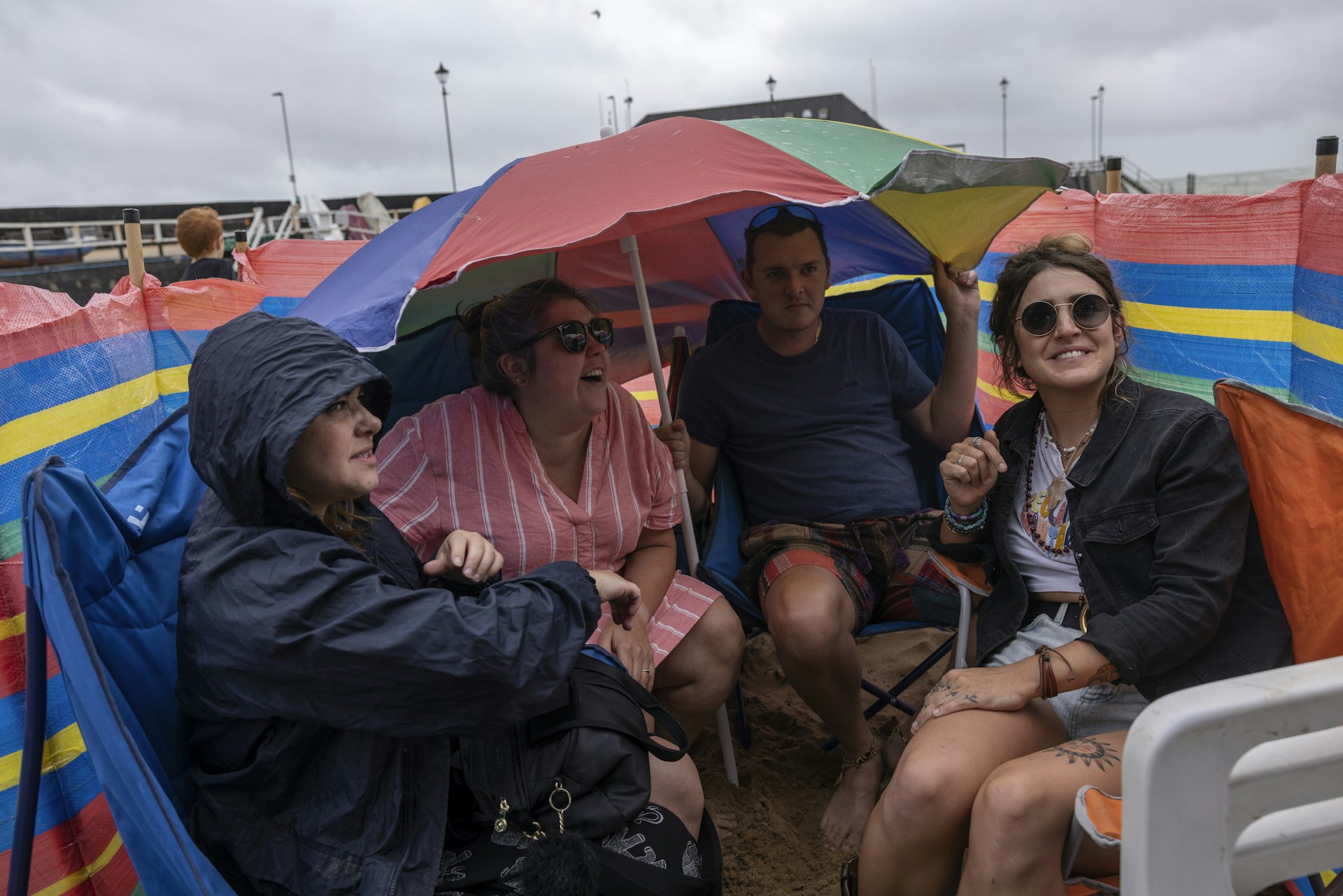 Friends shelter from the rain outside their beach hut in Broadstairs, England, United Kingdom,s