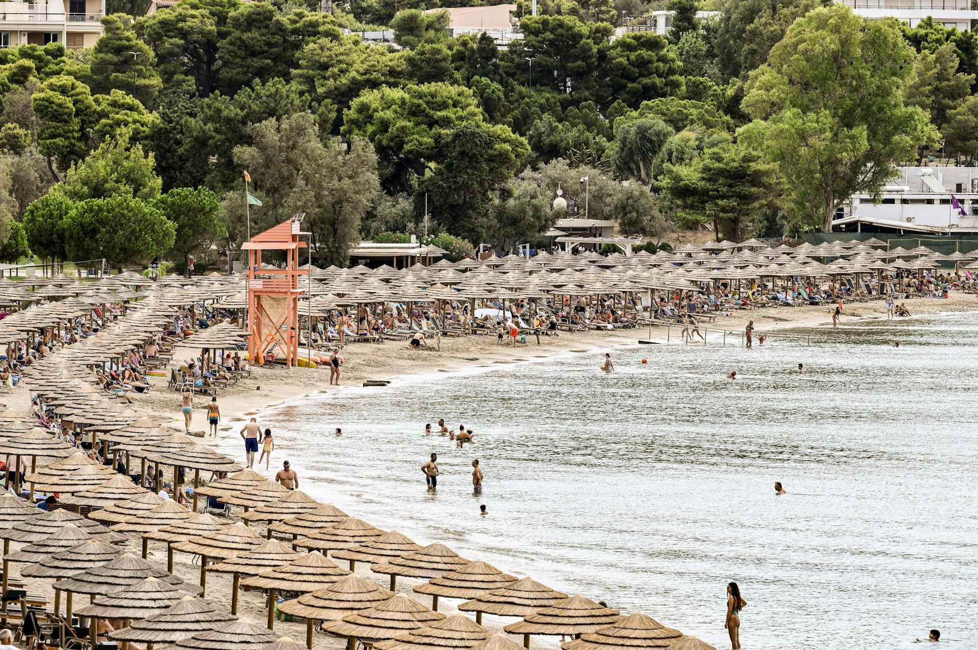 Beach-goers walk, lay and bathe on the Oceanis beach, as the area is covered by umbrellas and sun loungers