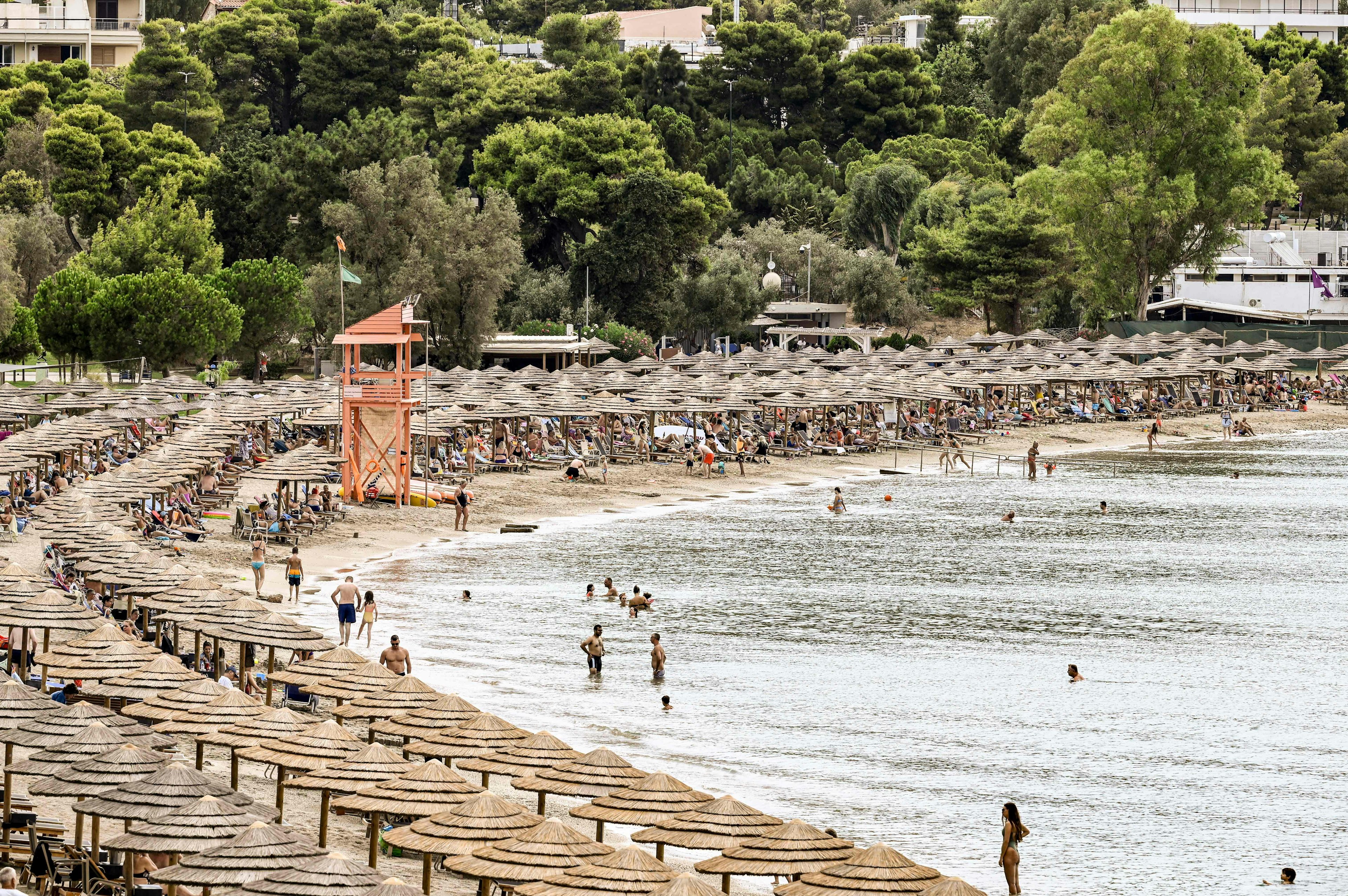 Beach-goers walk, lay and bathe on the Oceanis beach, as the area is covered by umbrellas and sun loungers