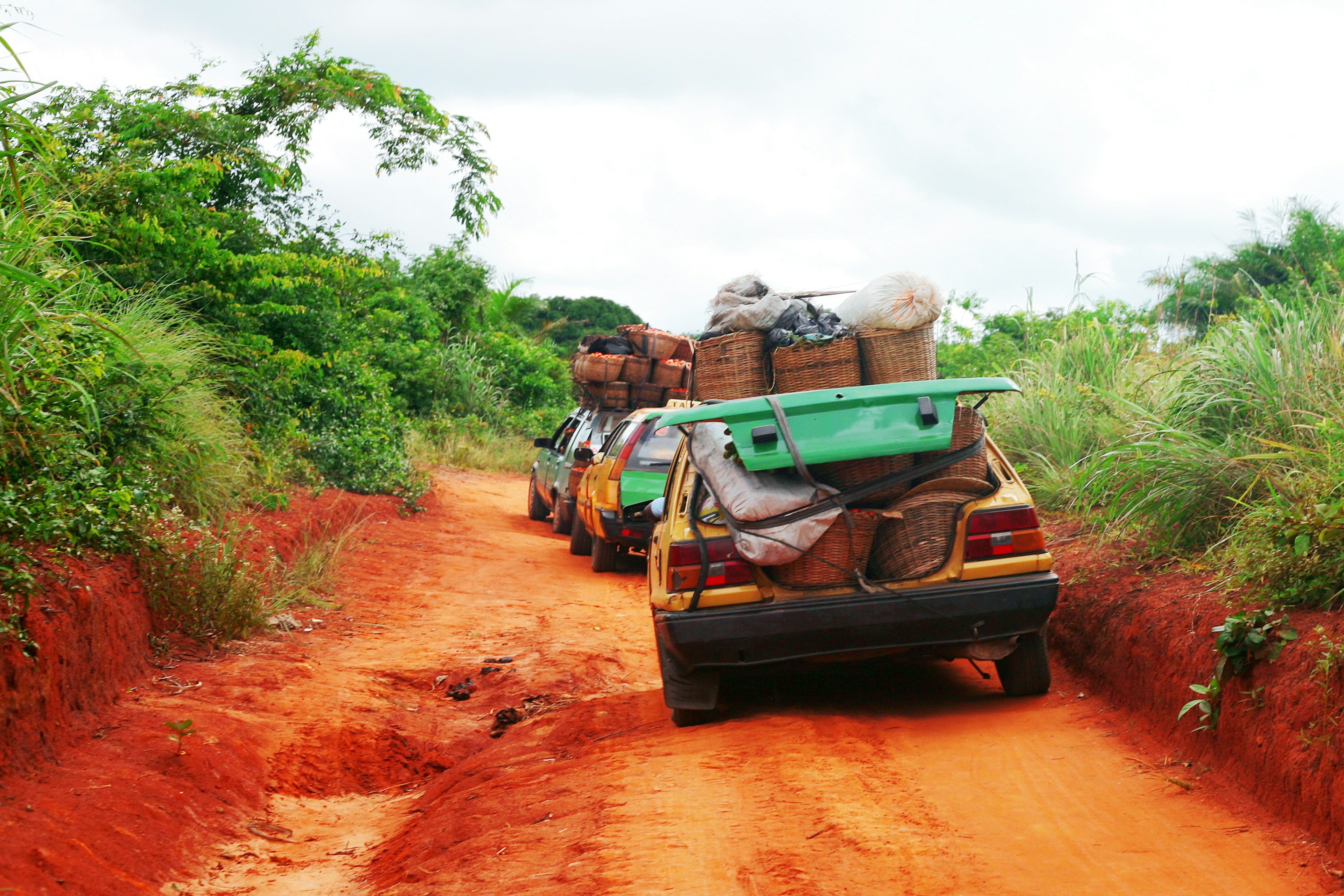 Three heavily loaded taxis drive down a dirt track