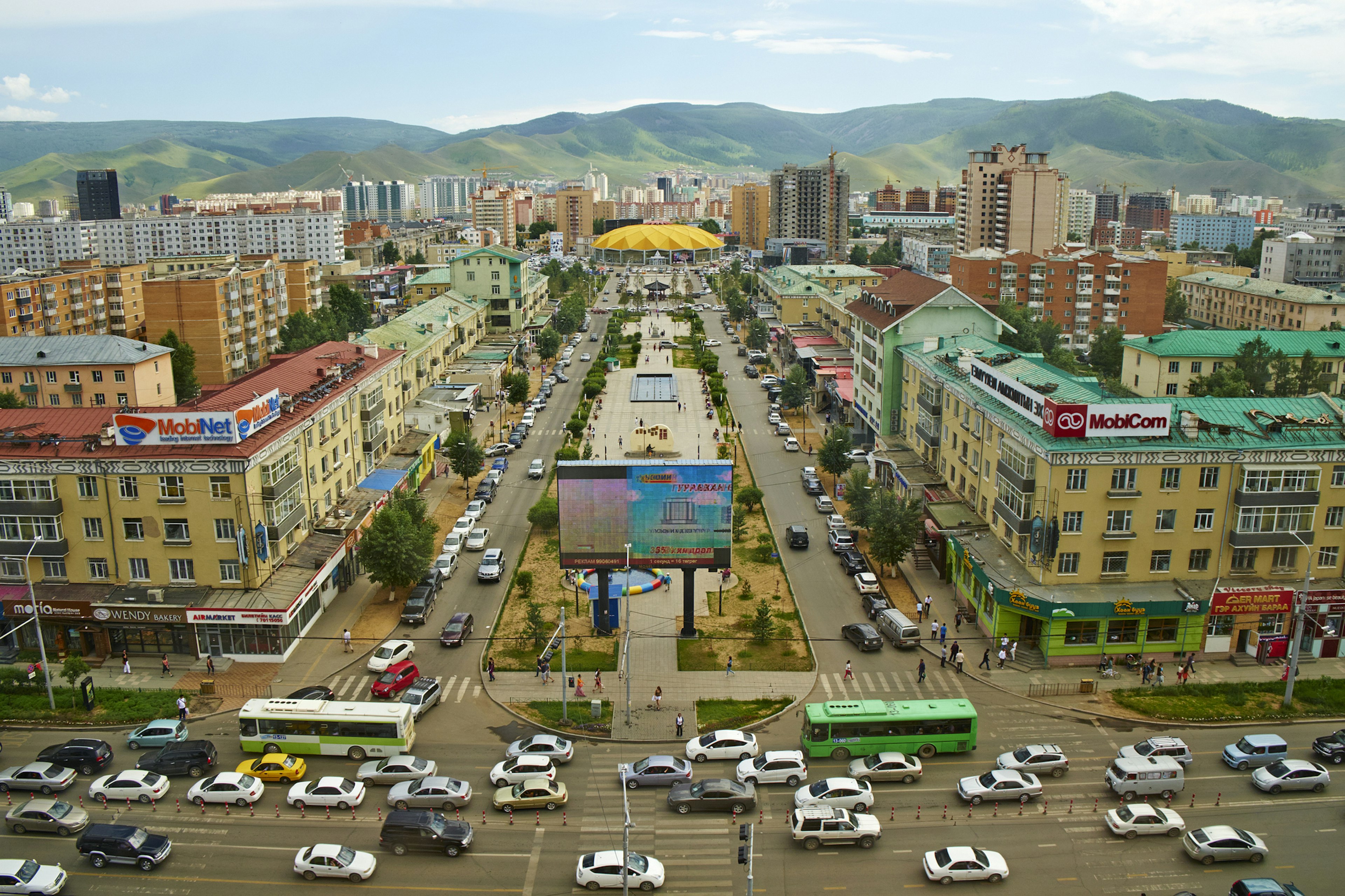 Streets and intersections are busy with vehicles in a city surrounded by hills