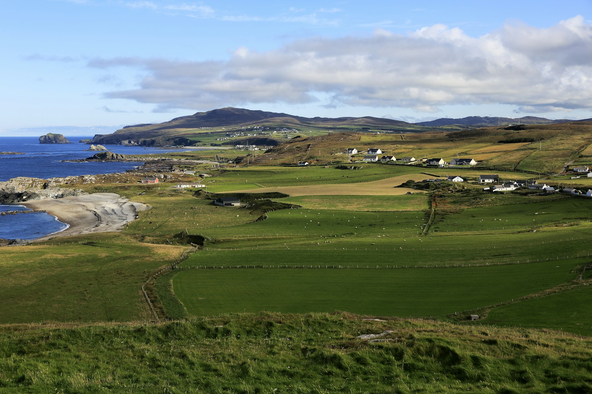 An aerial view of rolling green hills that sit alongside a rocky Irish shore at Malin Head