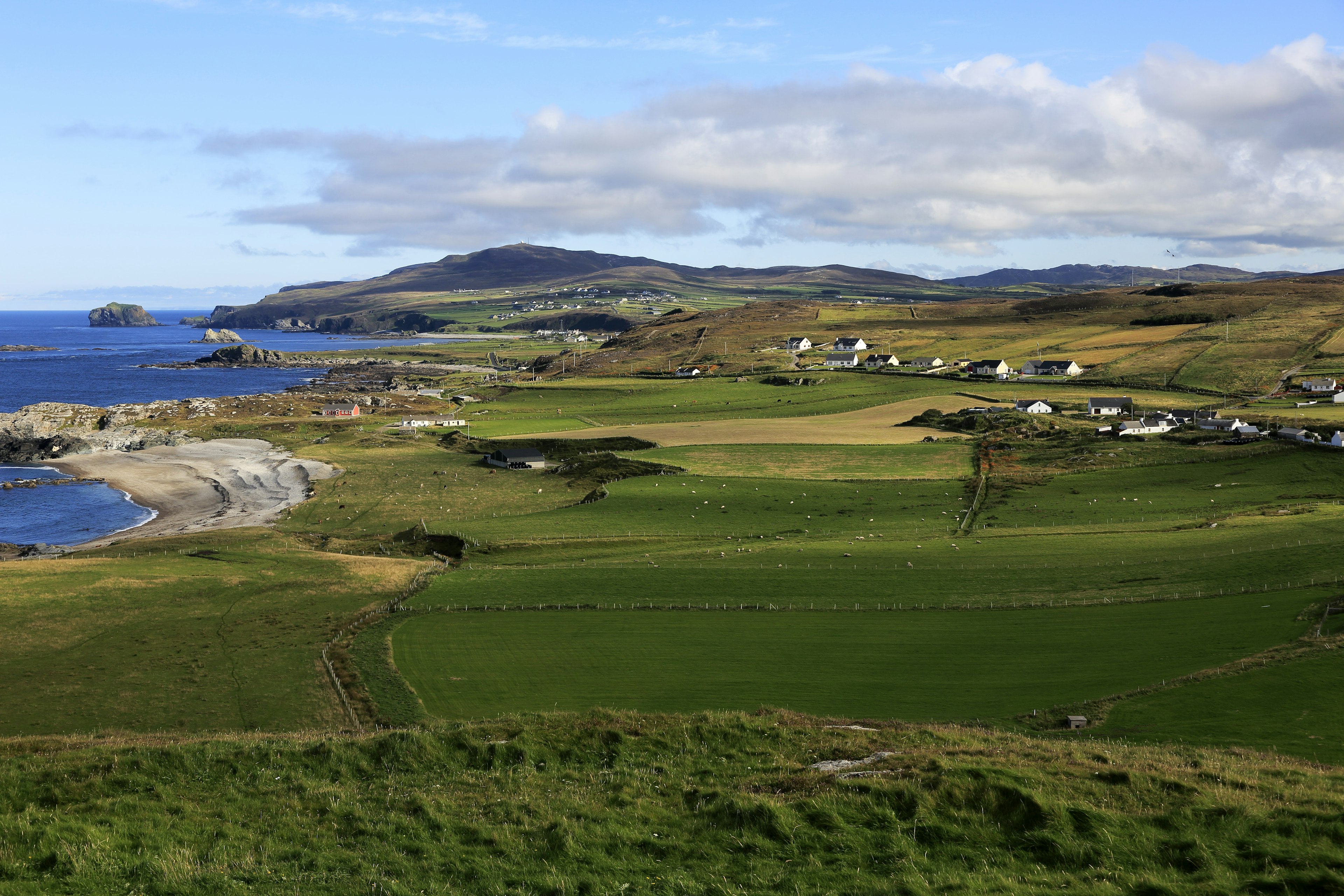 An aerial view of rolling green hills that sit alongside a rocky Irish shore at Malin Head