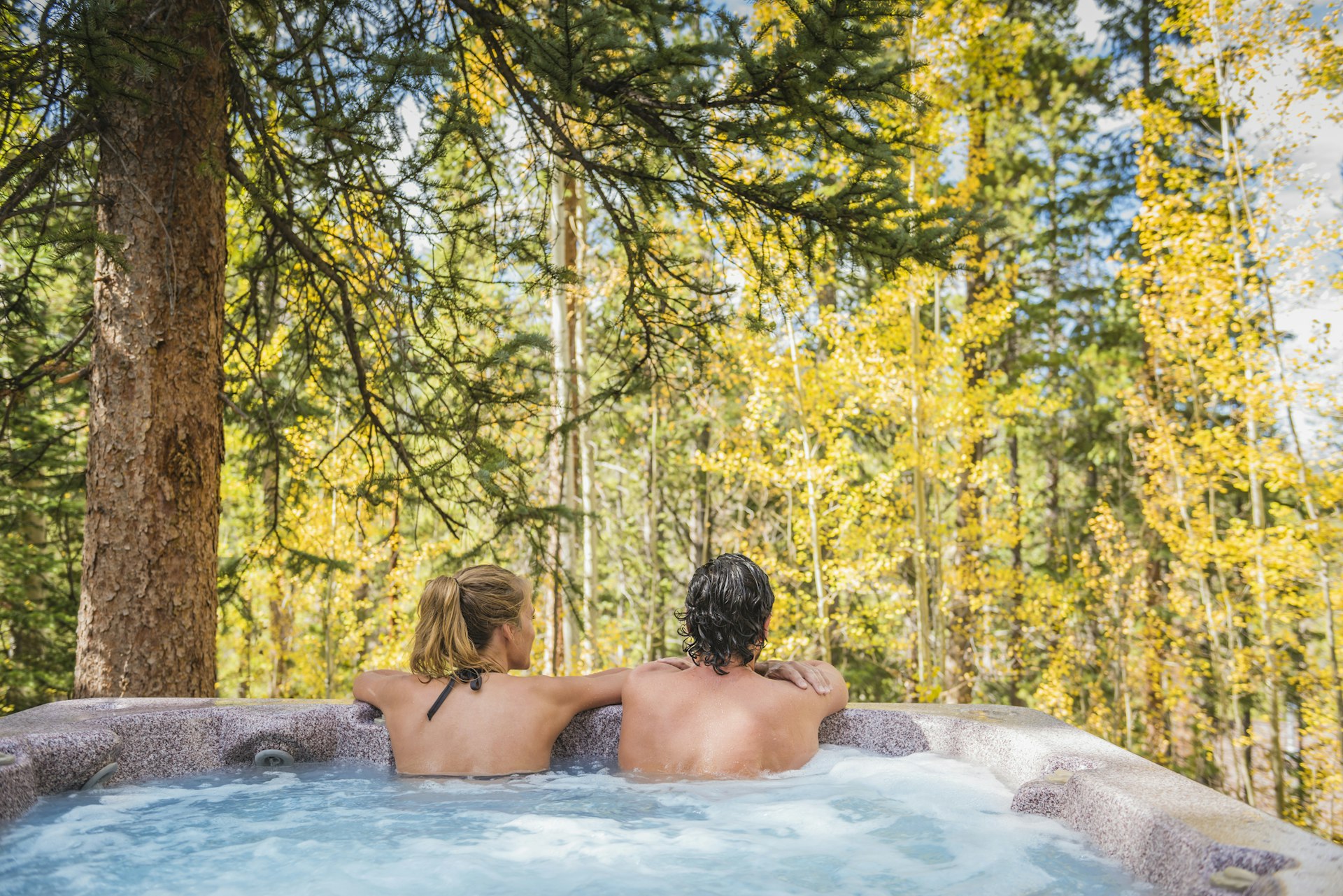 A couple lean on the edge of a hot tub gazing out into woodland