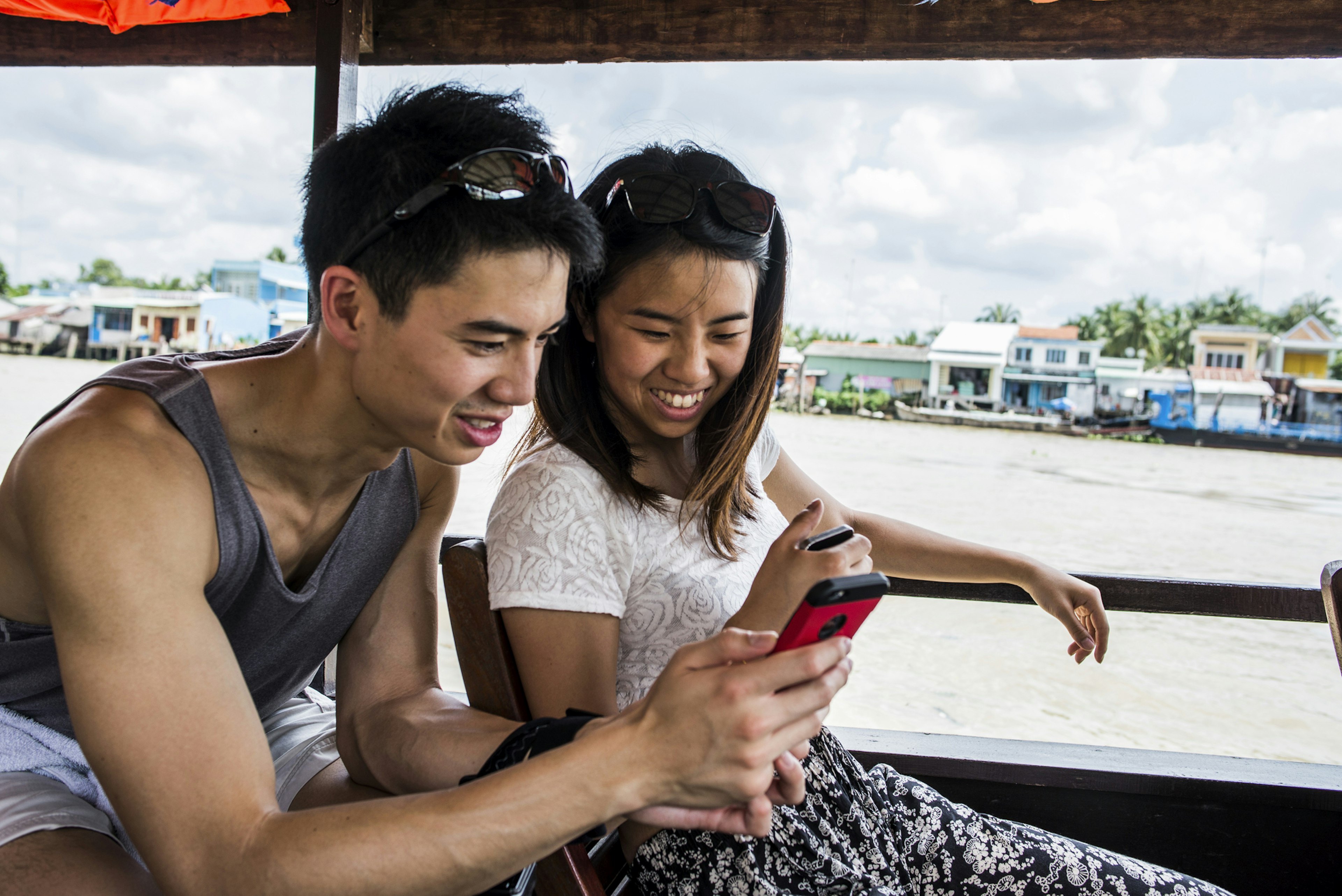 Two people on a boat look at cell phones and smile