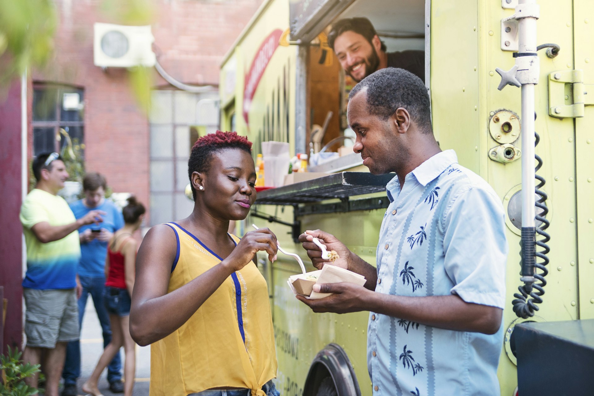 African-american couple enjoying their food from a food truck in city street. People in the background. Horizontal waist up outdoors shot with copy space. This was taken in Montreal, Canada.