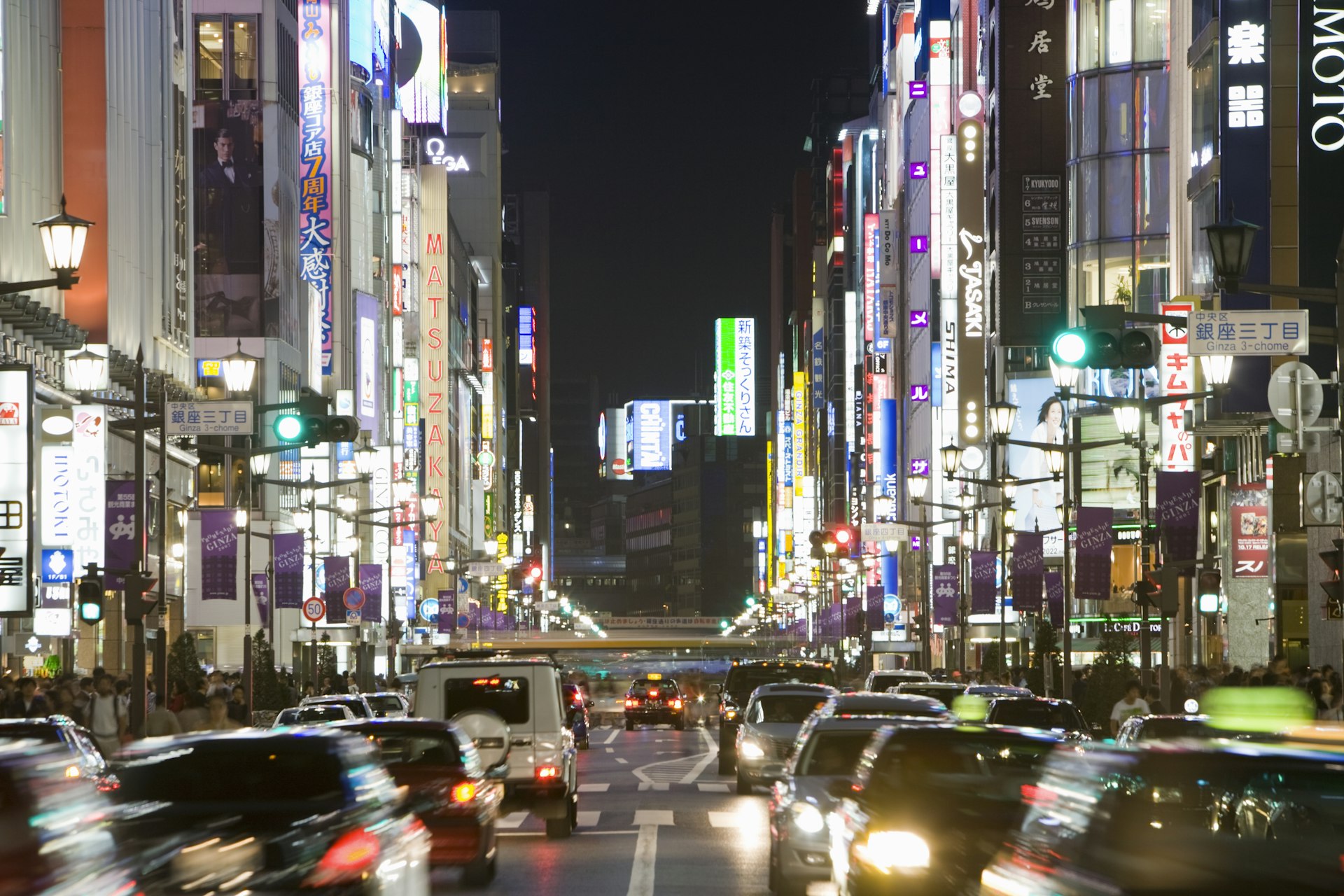 Chuo Street in Tokyo at night, very busy with traffic in motion, shops and signs are lit up