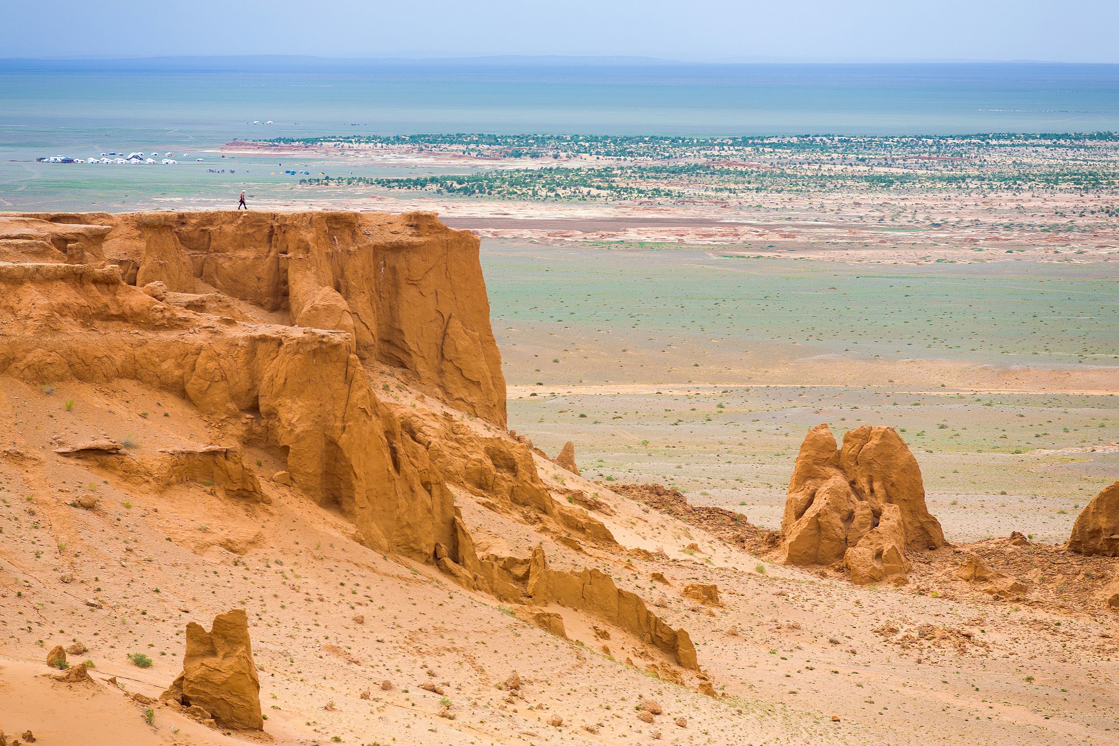 A distant figure walks on a raised flat rock in the middle of a vast desert