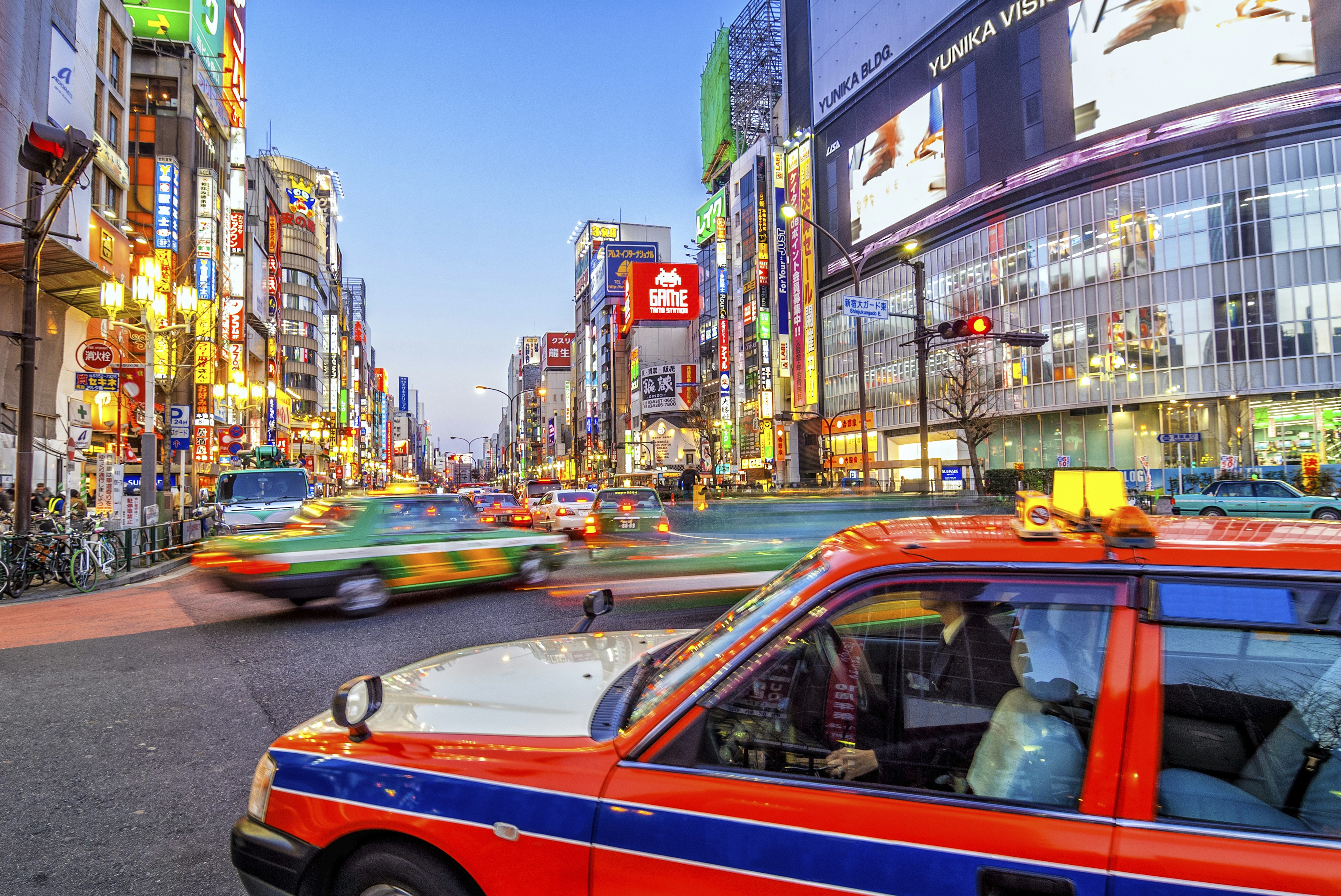 Tokyo taxi turning right in a busy road, traffic ahead has motion blur, the shops have neon billboards