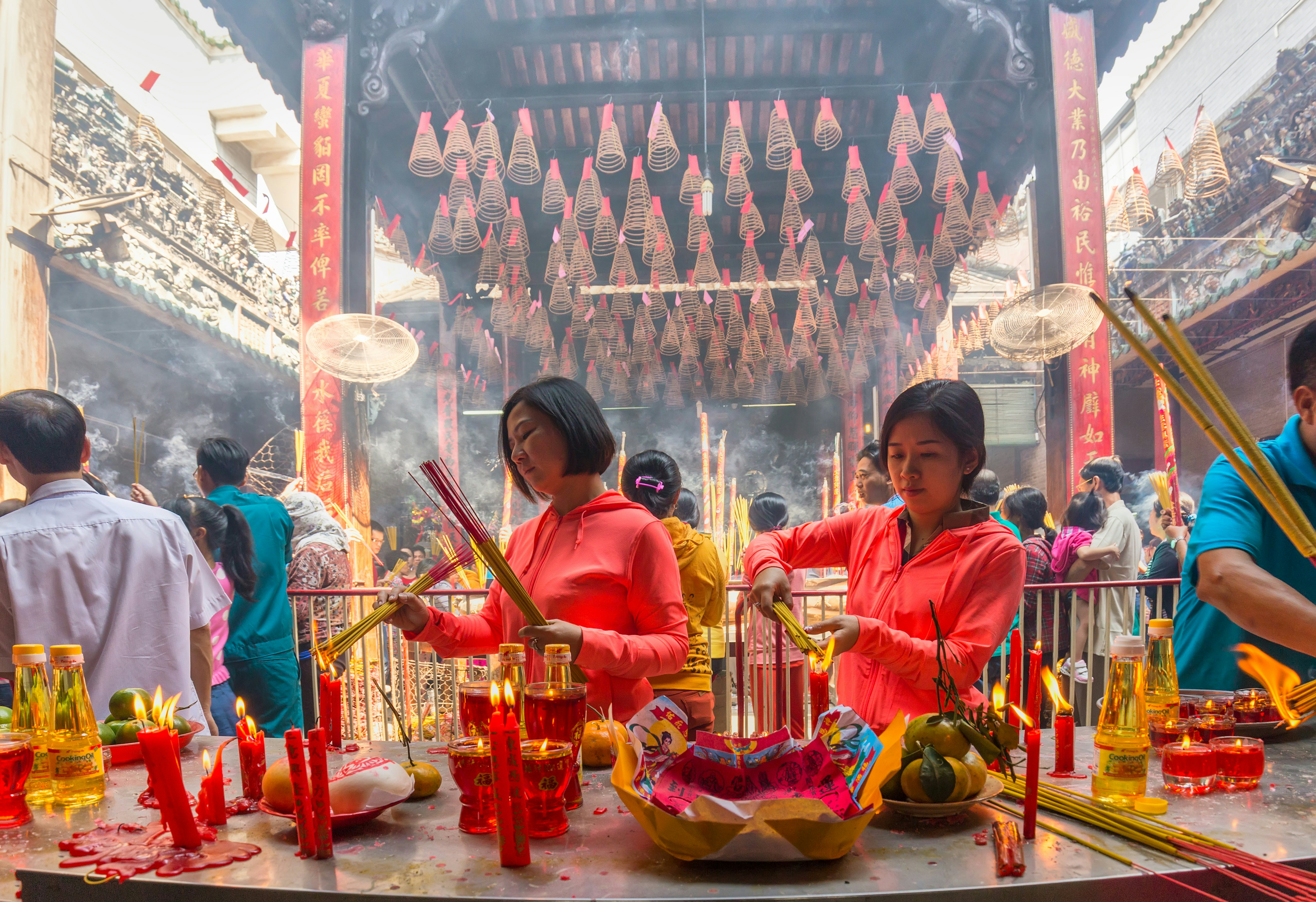 Two women wearing red shirts burn incense at a temple during Lunar New Year in Vietnam