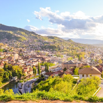Aerial of Sarajevo during spring on a sunny day.
528720648
Above, Travel, Modern, Sarajevo, Spirituality, Access, Mountain Peak, Light - Natural Phenomenon, Photography, Overcast, Blue, Summer, Road, Clear Sky, Ottoman Empire, Religion, Rooftop, Town, On Top Of, Horizon Over Land, Accessibility, Sun, Sky, Multi-Ethnic Group, Landscape - Scenery, Viewpoint, Landscape, Bosnia and Hercegovina, Cityscape, Architecture, Famous Place, Old, Day, Horizontal, Europe, Tourism, Haze, Awe, Street, History, Journey, The Past, Transparent, Cultures, Multi Colored, 60595, Sunset, Sunlight, Vibrant Color, Capital Cities, City Life, Outdoors, High Angle View, Aerial View, Cloud - Sky, Horizon, Fog, City
