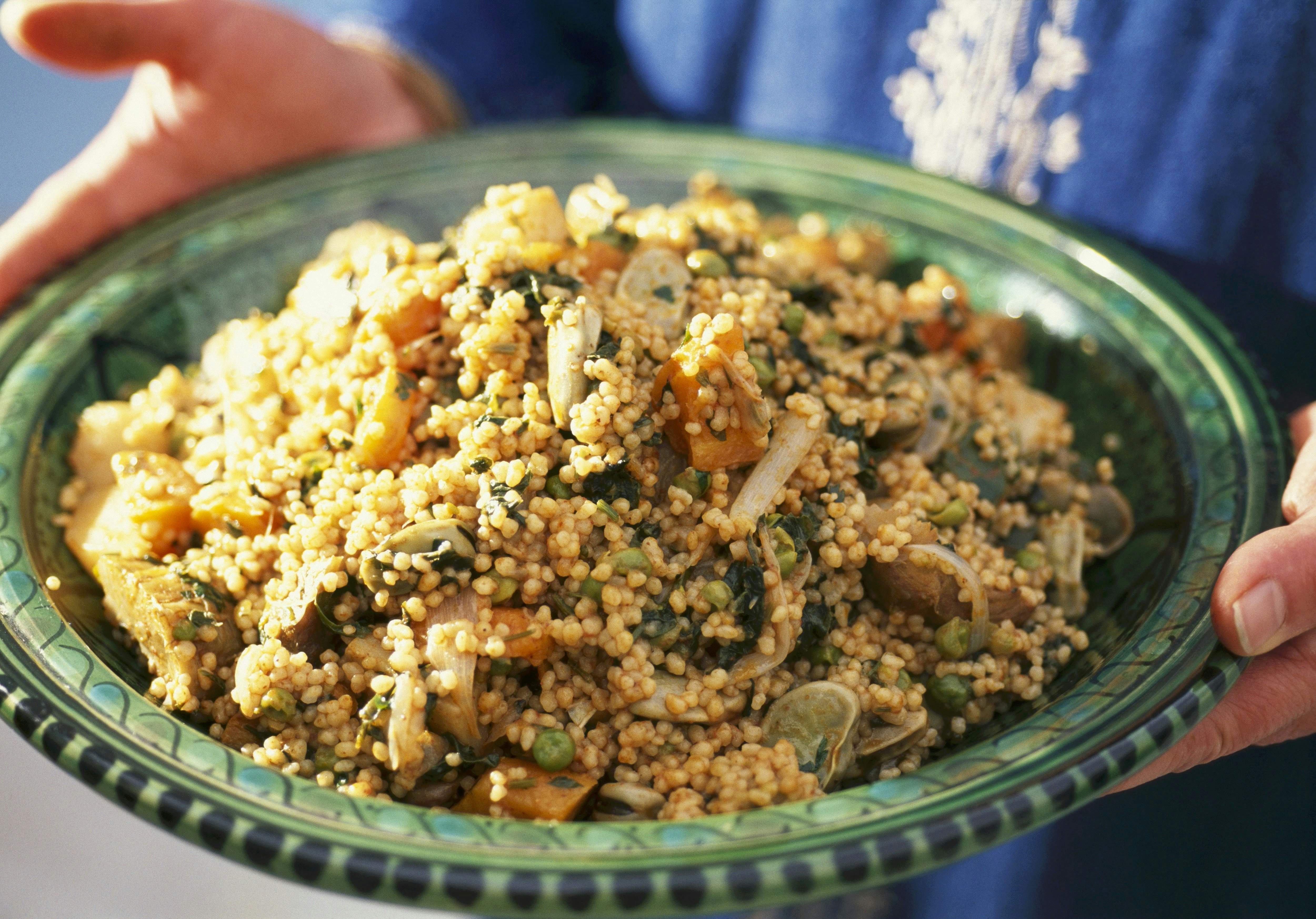 Person holding a green dish of vegetable couscous