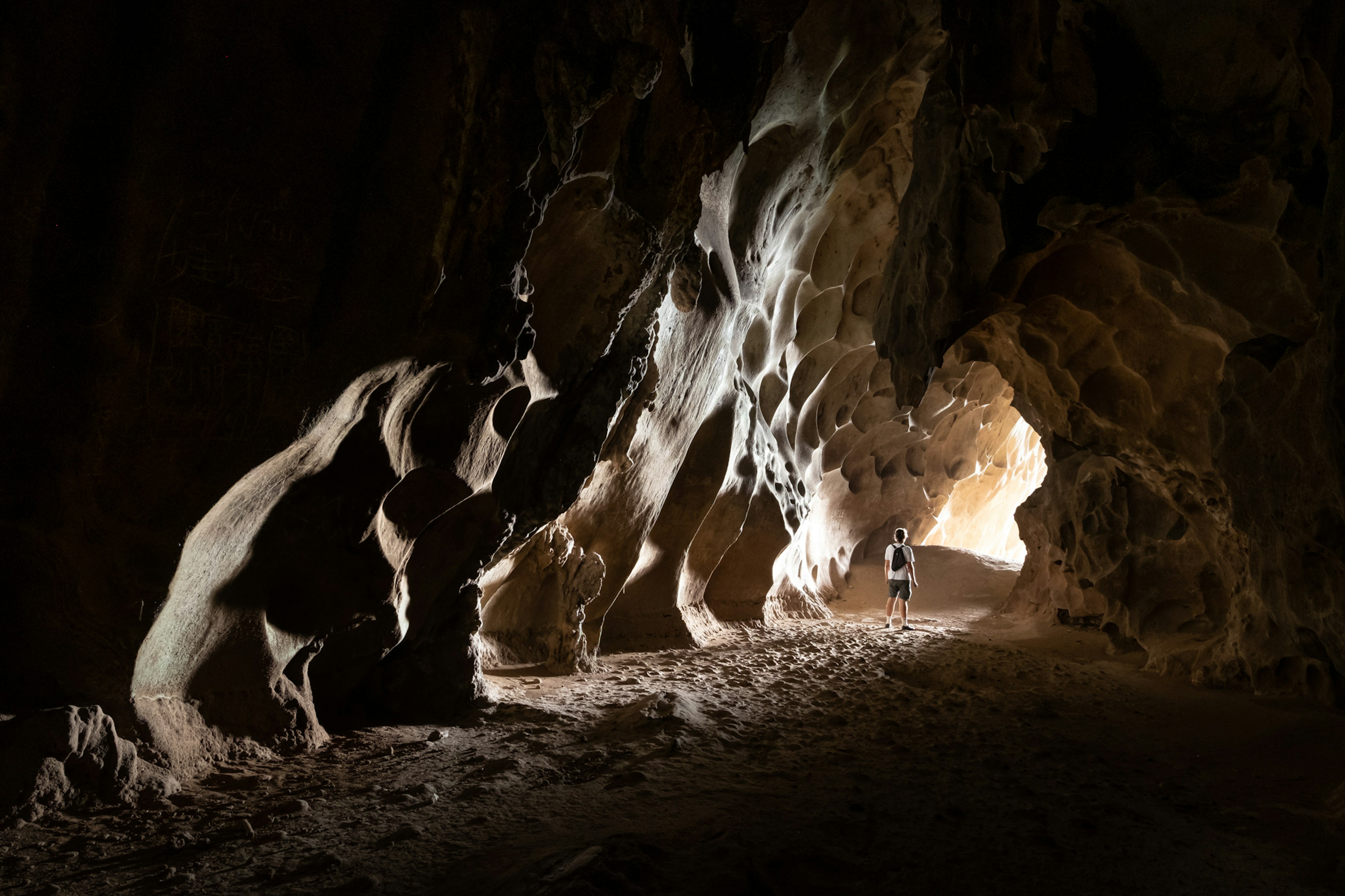 A person stands in the opening of a cave, as light penetrates to reveal sculptural calcite formations