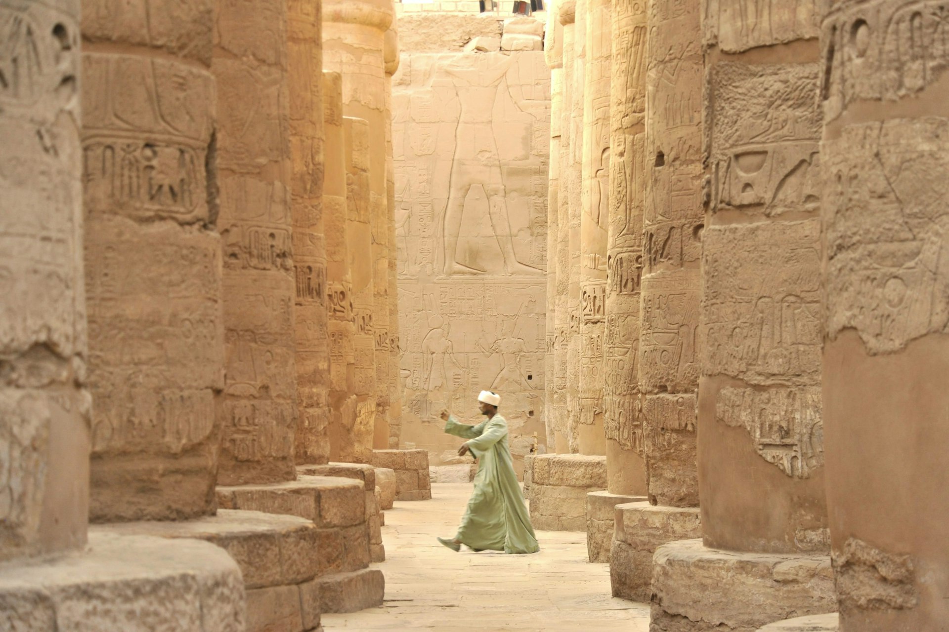 Egyption man walking through the towering pillars of the Karnak Temple.