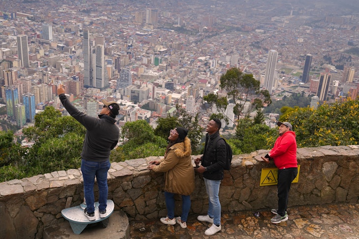 A man standing on a step at the top of Cerro de Monserrate taking a selfie with friends with Bogotá in the background