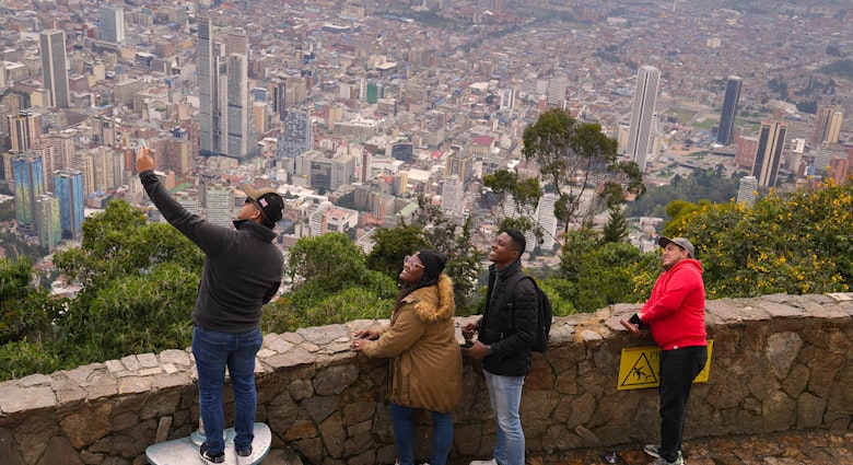 A man standing on a step at the top of Cerro de Monserrate taking a selfie with friends with Bogotá in the background