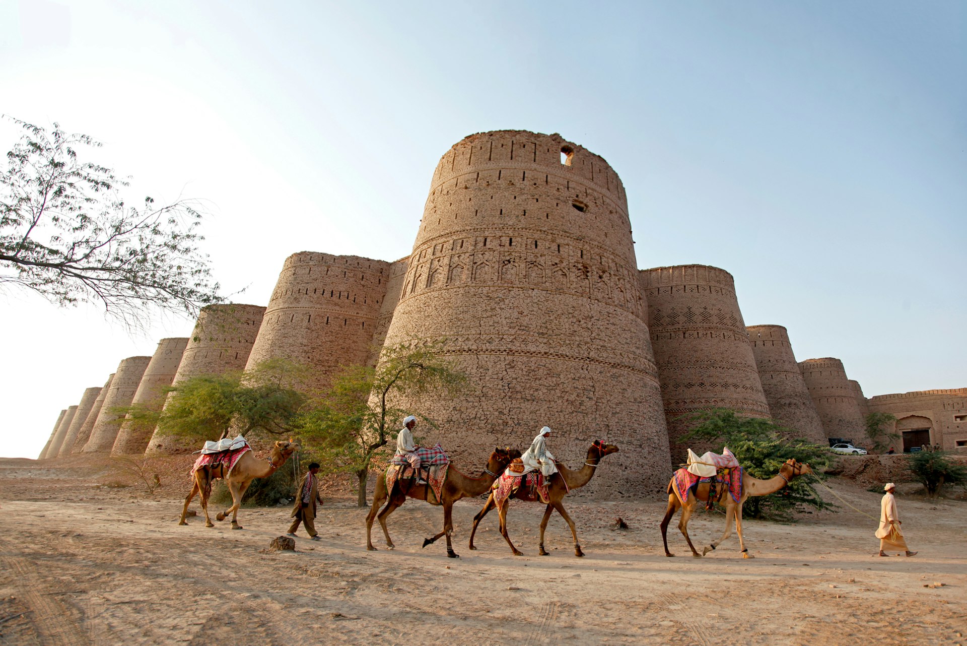 Riders on camels pass a fort in rural Pakistan