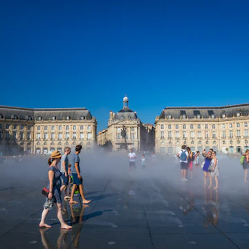 Visitors having fun on the Mirroir d'eau (Water Mirror) of the Place de la Bourse in Bordeaux, France on a hot summer day during a heat wave.