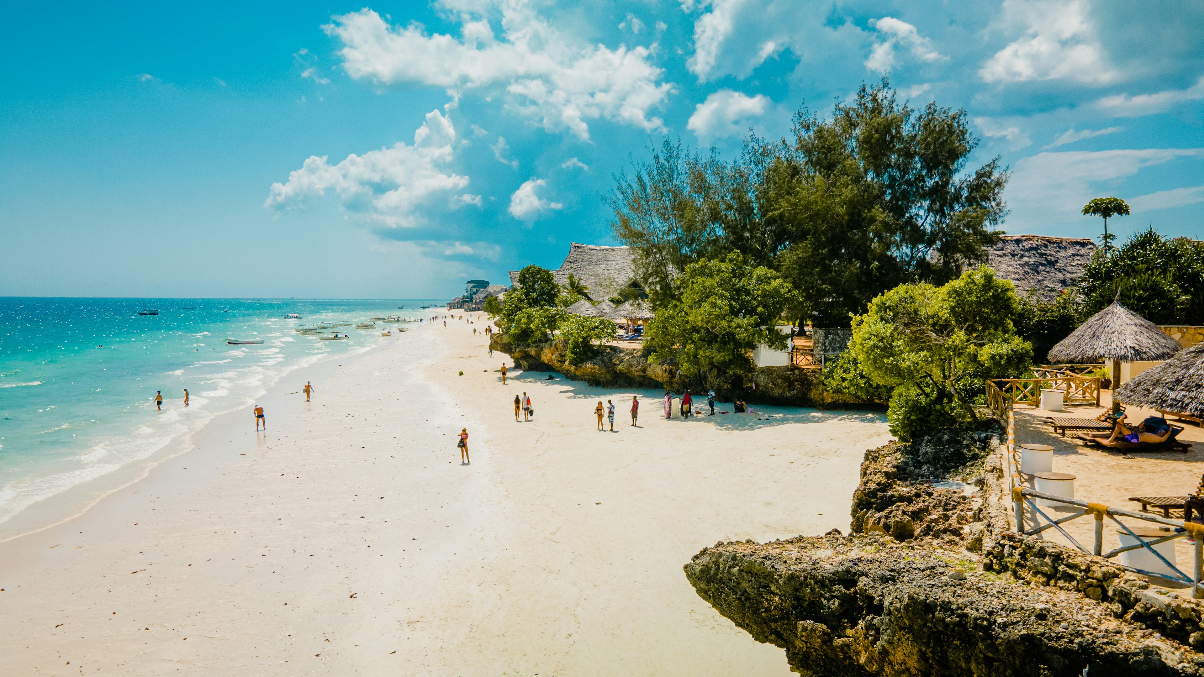 People on a white-sand beach backed by straw huts