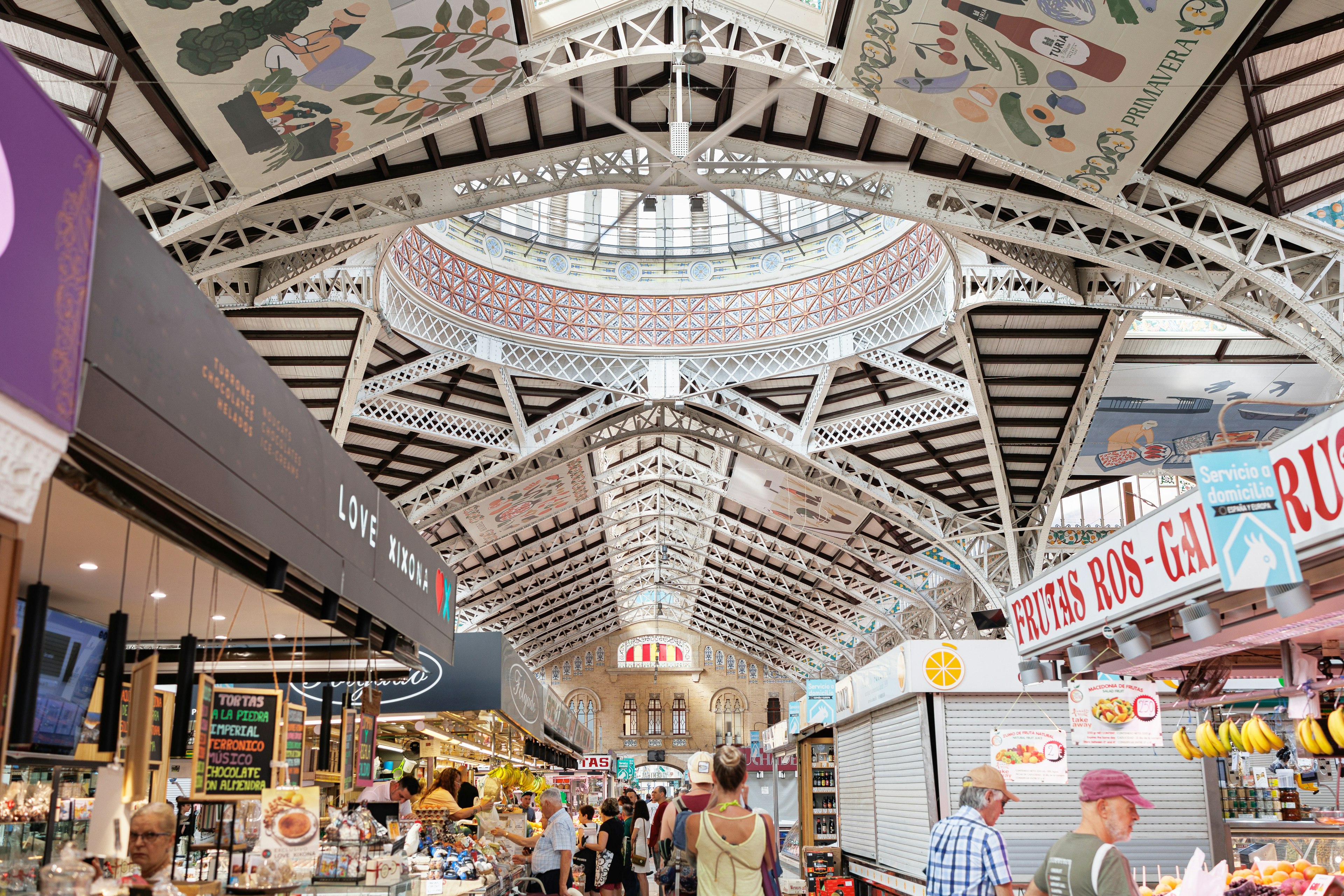 A few of the painted cast-iron beams and domes of the Modernista Mercado Central with shoppers and vendors, Valencia, Spain