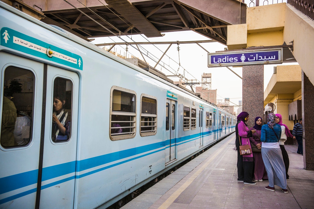 Four women stand together on the platform under a sign that says