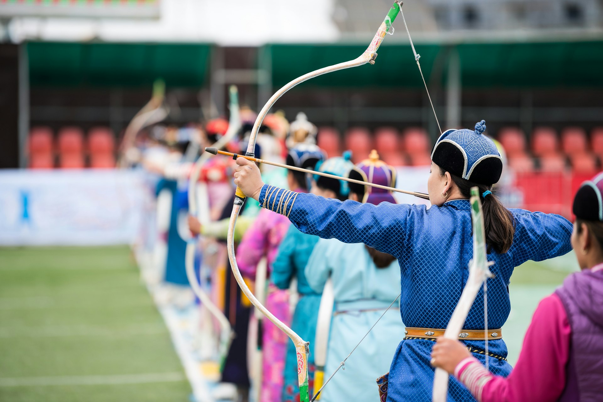 A woman in traditional Mongolian dress takes aim with a bow and arrow during an archery contest