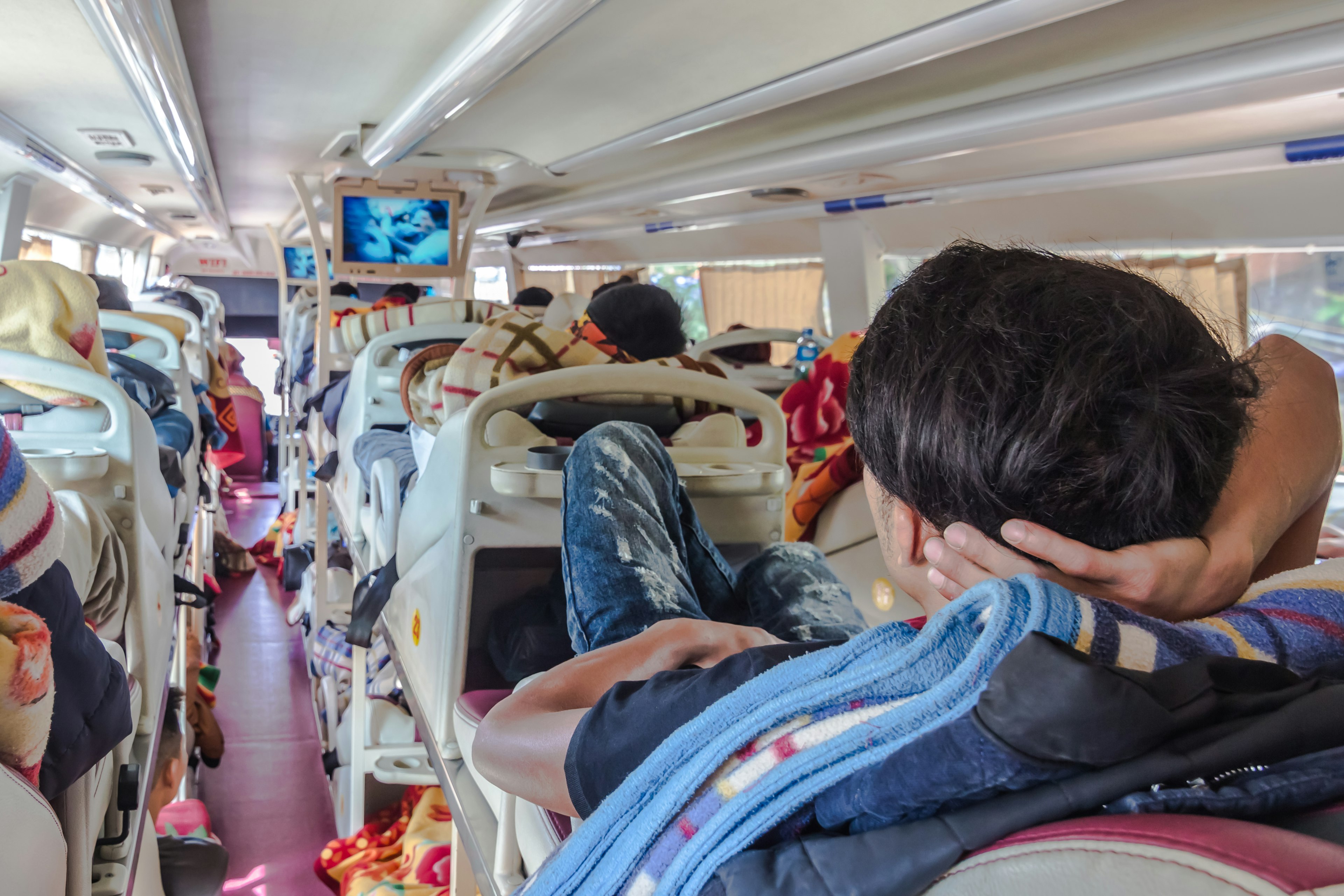 A man reclining in a seat and watching TV on a long-distance sleeper bus