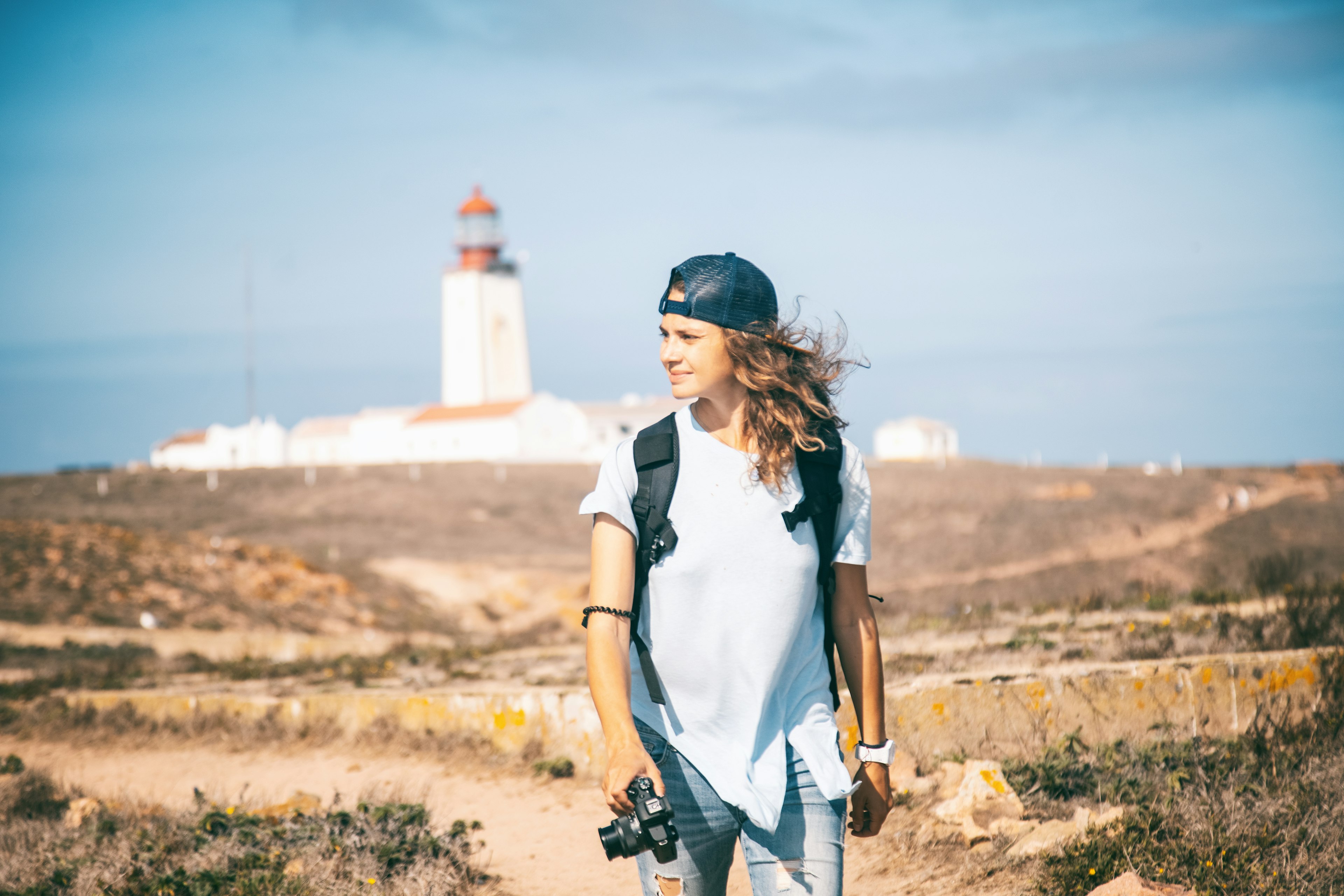 A photographer walks along a trail in a nature reserve with a lighthouse in the background