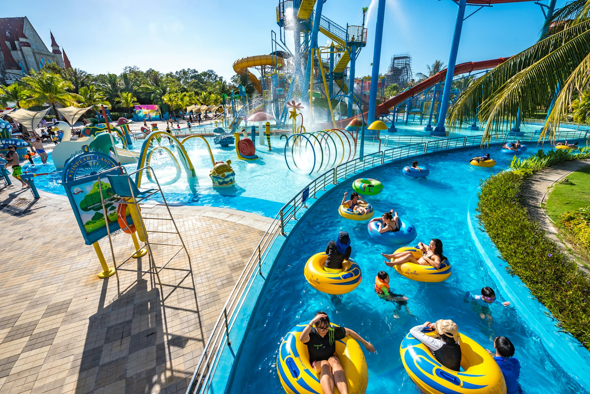 People float along in yellow rubber rings at a water park with lots of splash pools and slides