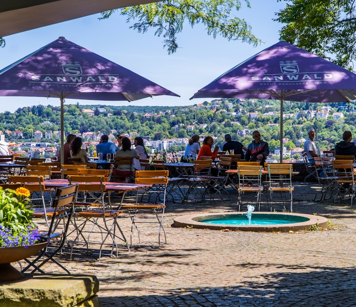 People drinking and eating in a beer garden on the Karlshöhe hills with panoramic Stuttgart city view in the background