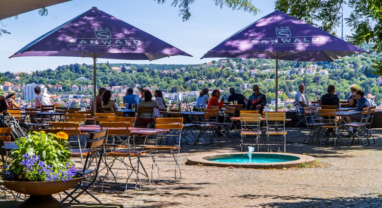 People drinking and eating in a beer garden on the Karlshöhe hills with panoramic Stuttgart city view in the background