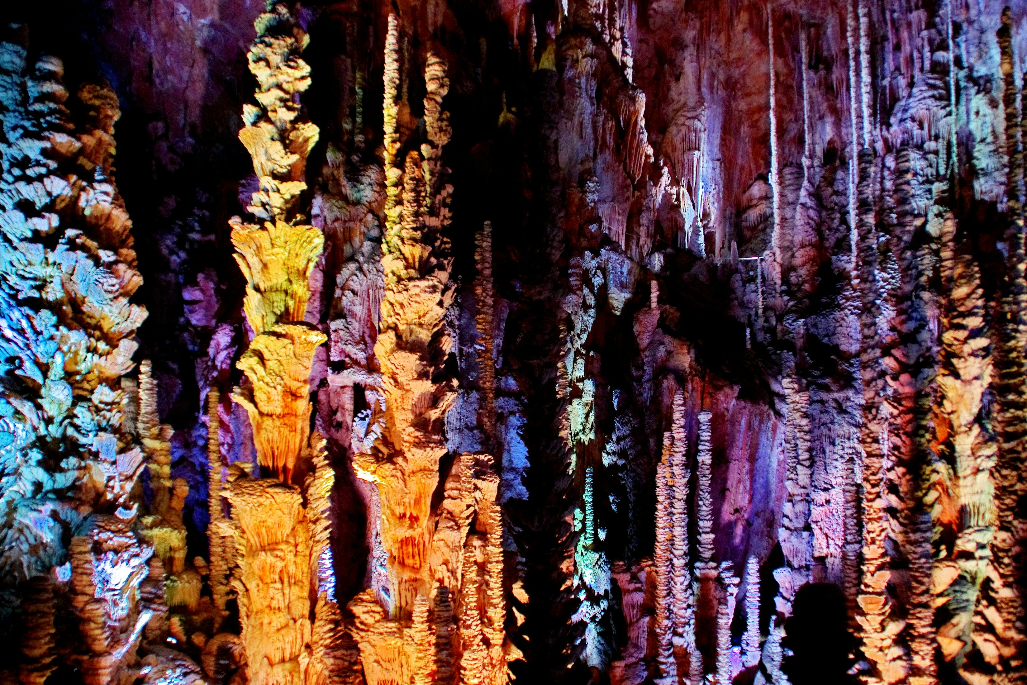 Stalactites and stalagmites lit with multicolored lights in the Aven Armand cave.