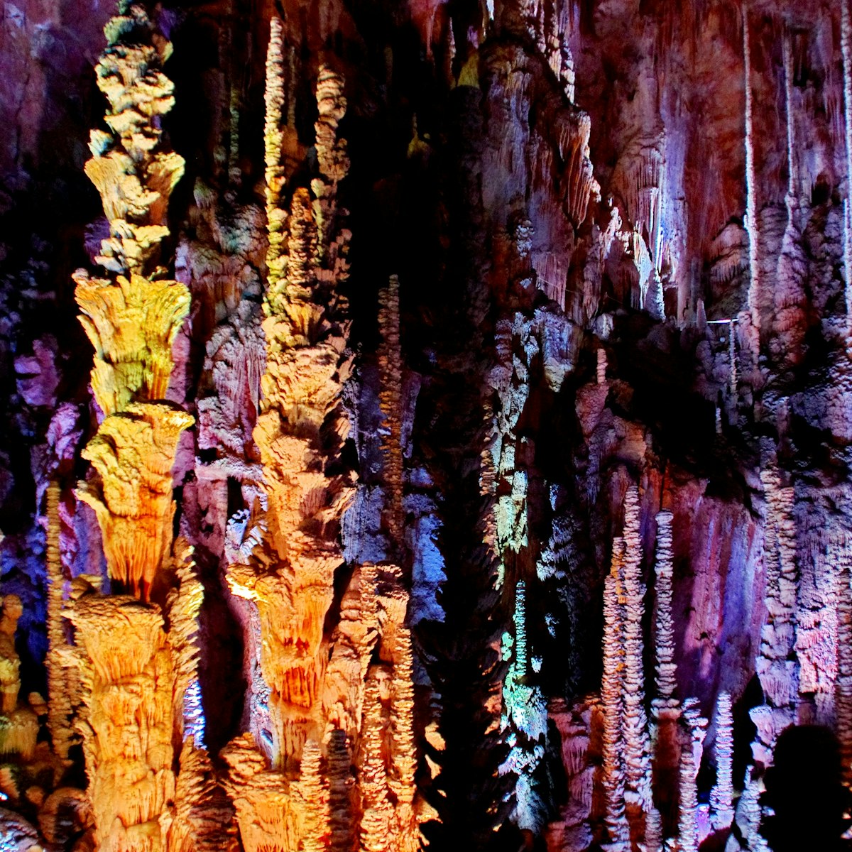 Stalactites and stalagmites lit with multicolored lights in the Aven Armand cave.