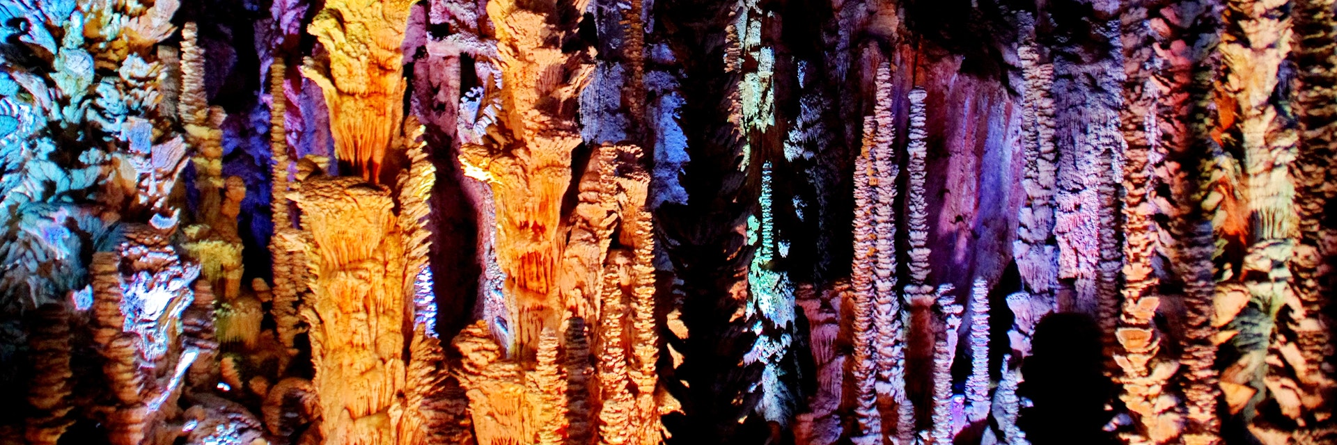 Stalactites and stalagmites lit with multicolored lights in the Aven Armand cave.