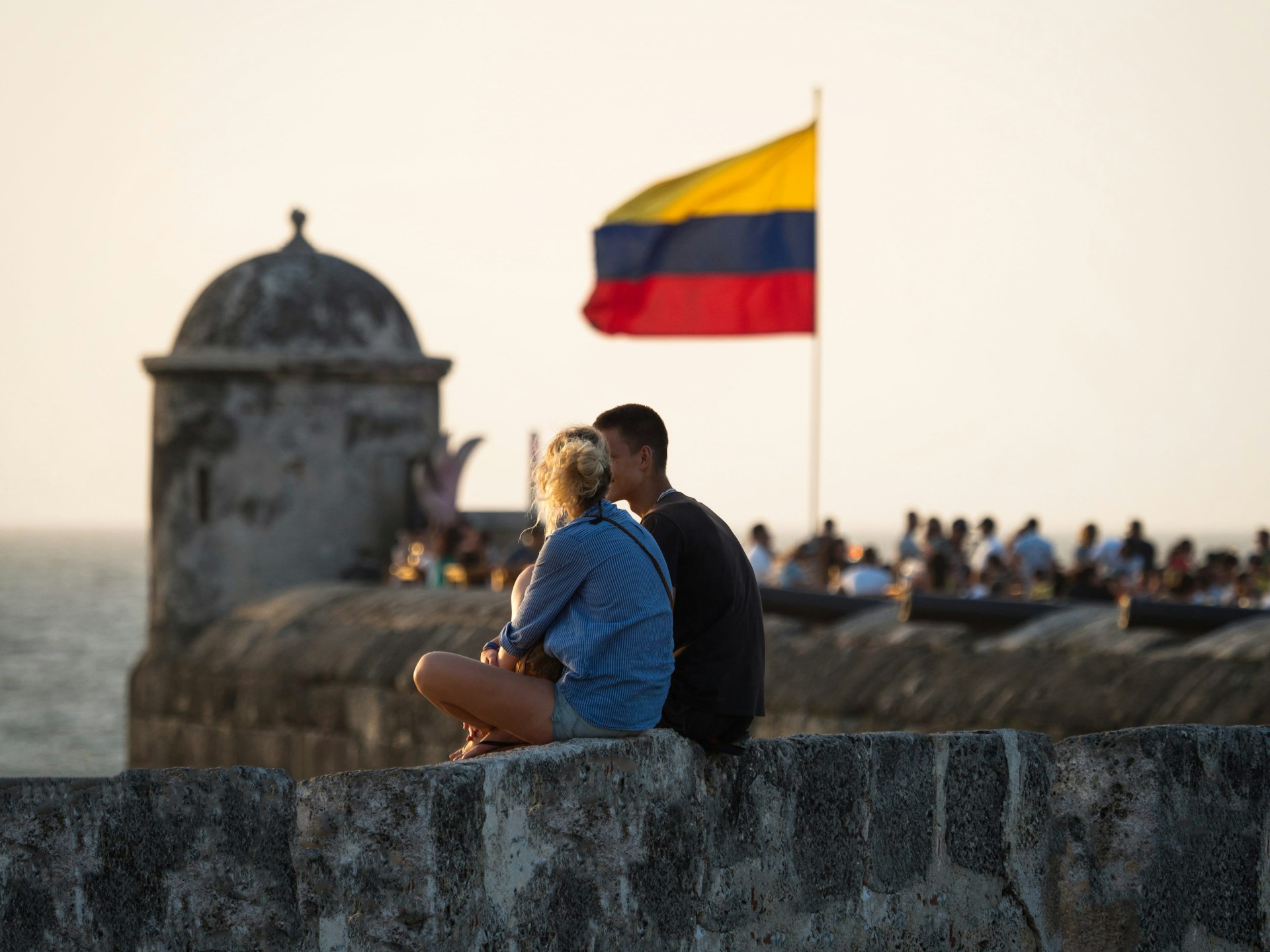 A couple sits on a city wall watching the sunset with the Colombian national flag waving in wind