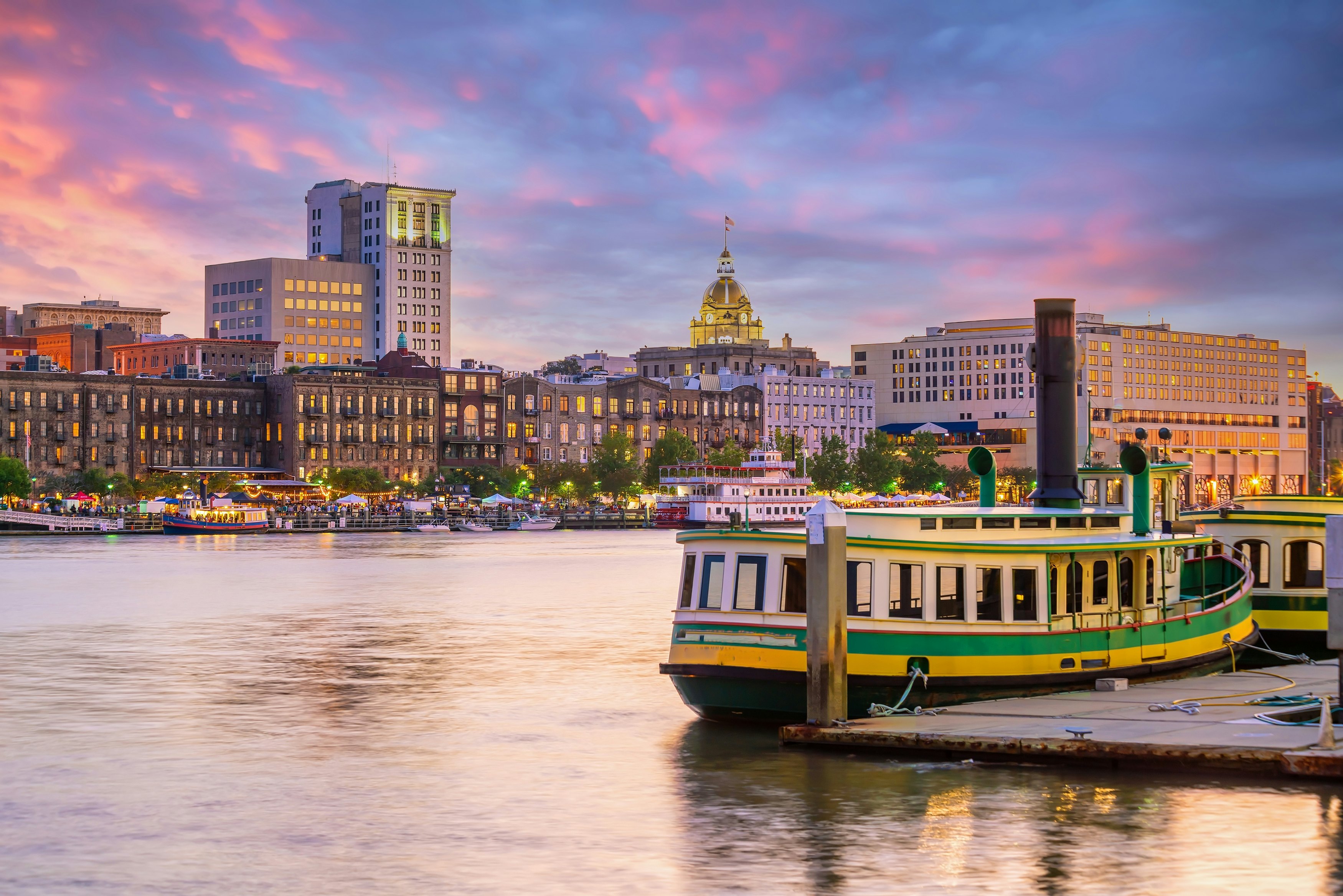 Ferries are docked along the historic district waterfront of Savannah, Georgia USA at sunset.