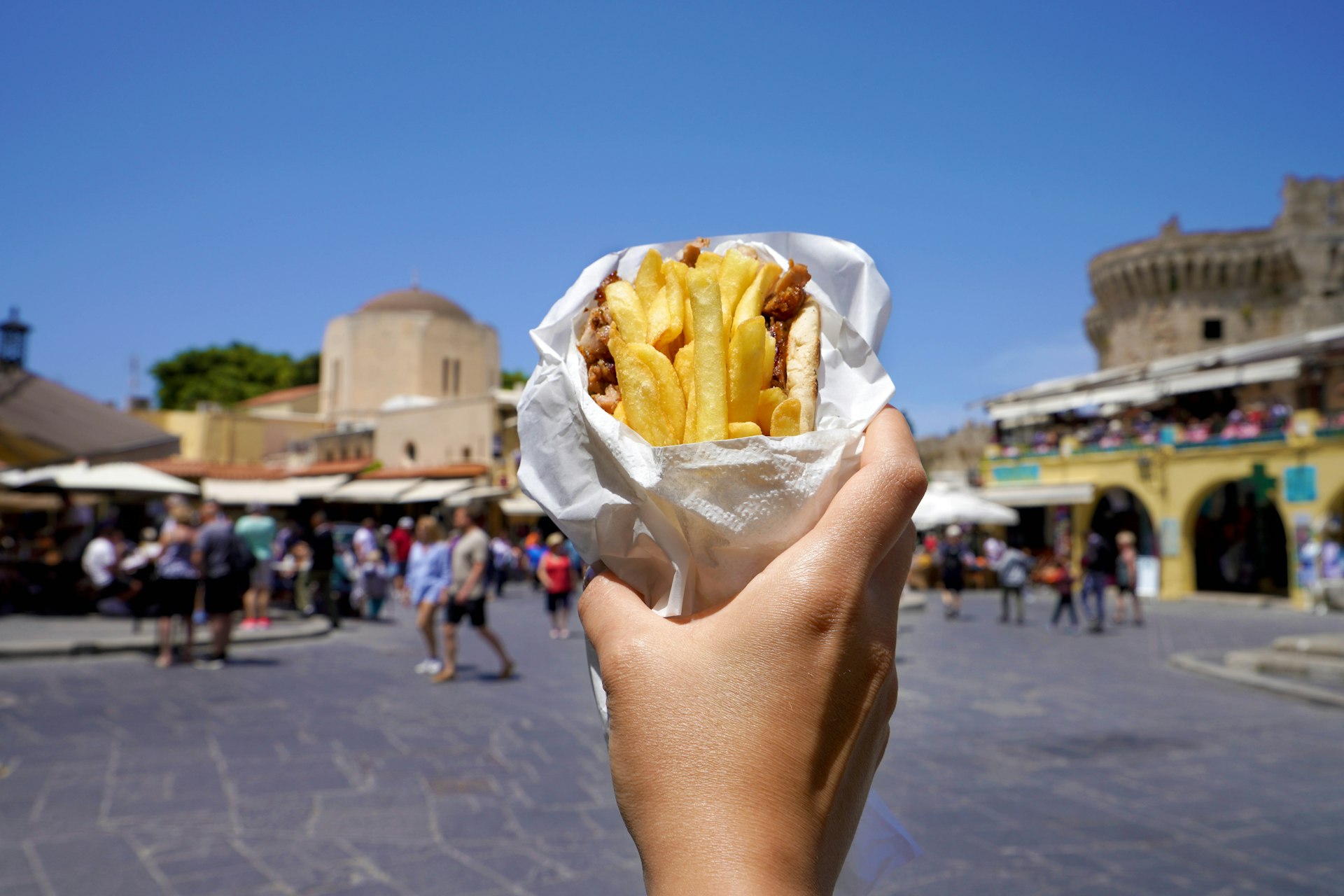 Greek gyros wrapped in pita bread and held up against the background of a Greek old city square