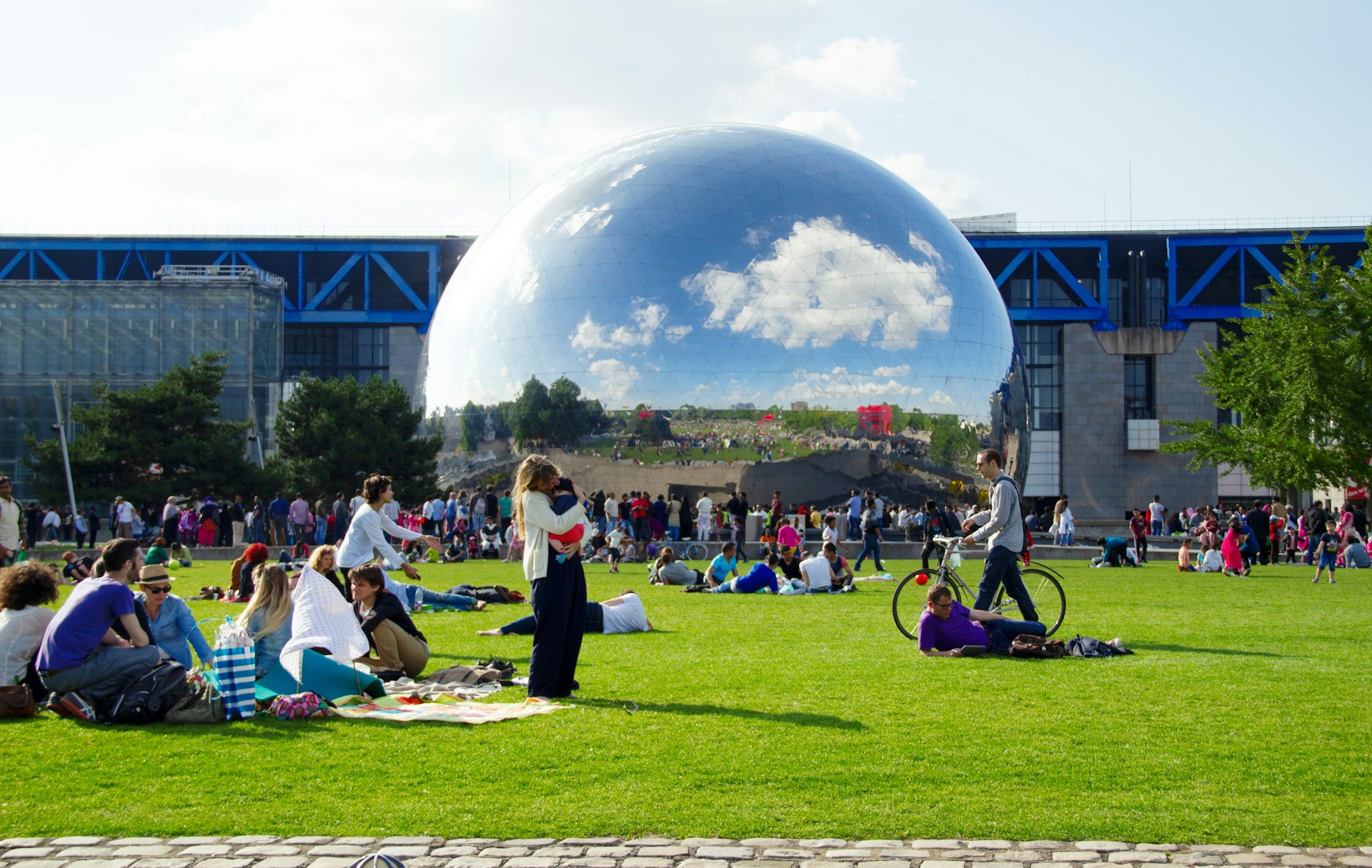 People gather in a park in Paris nearby a huge silver sphere, part of the Cité des Sciences