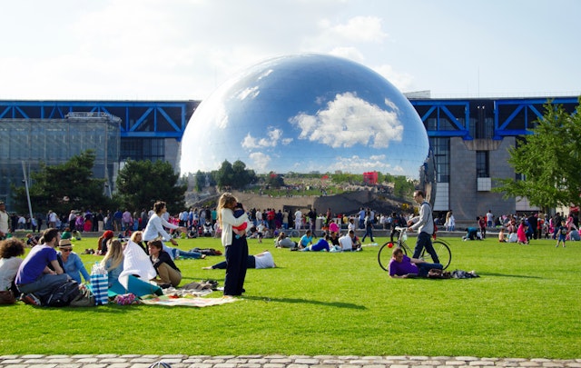 People gather in a park in Paris nearby a huge silver sphere, part of the Cité des Sciences