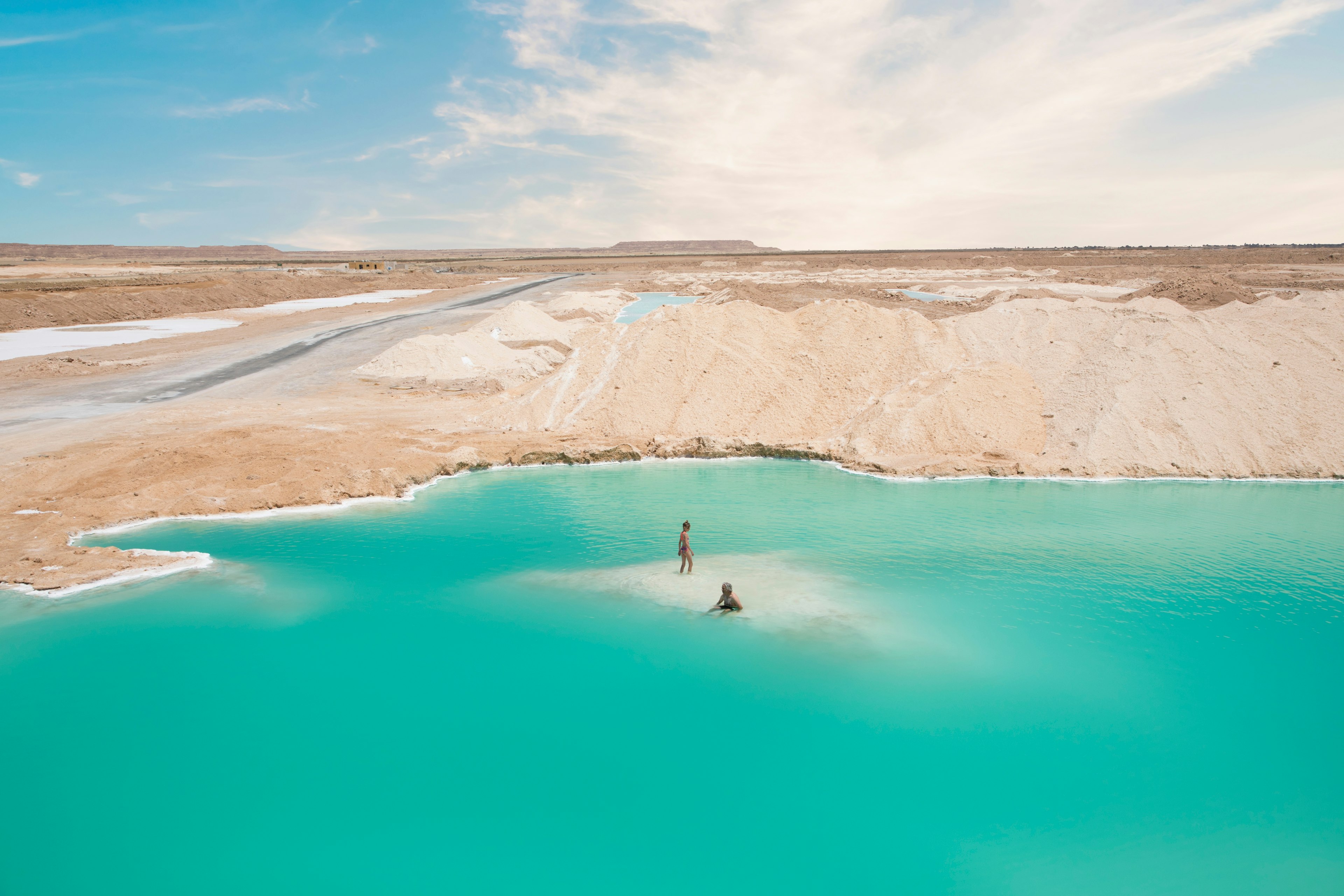 Two people in a turquoise salt-filled lake on the edge of desert