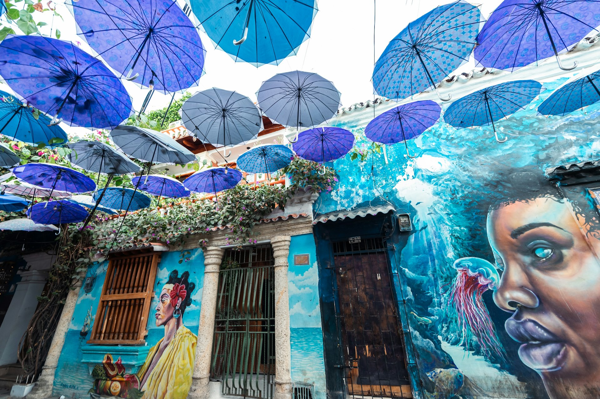 Street art in shades of blues, greens and purple is complemented by decorative umbrellas hanging in the street above head height