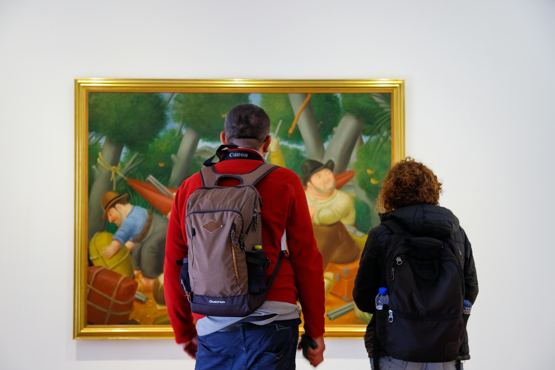 Two people stand in an art gallery facing a painting of large figures