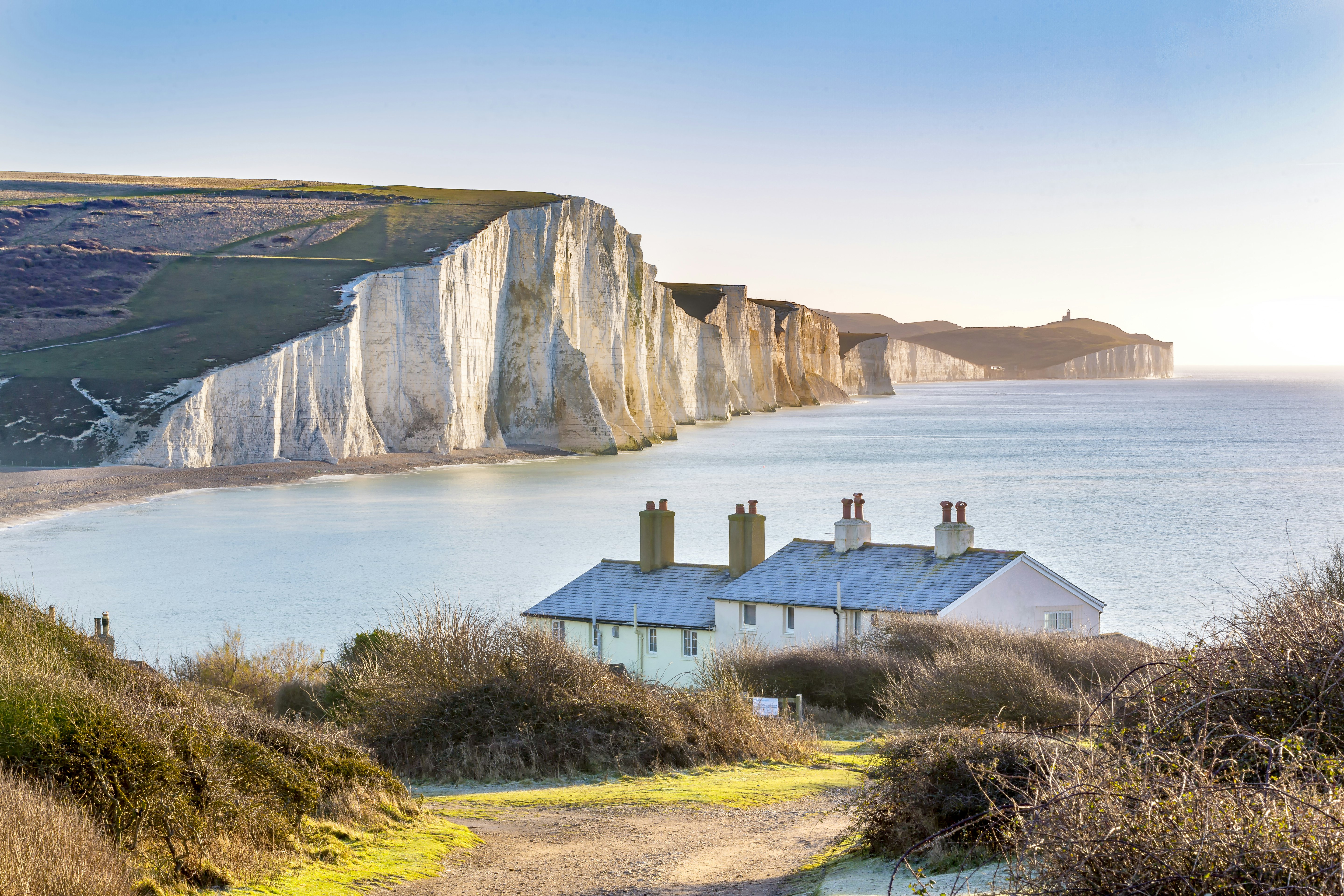 A small row of coastal cottages backed by dramatic rolling white cliffs