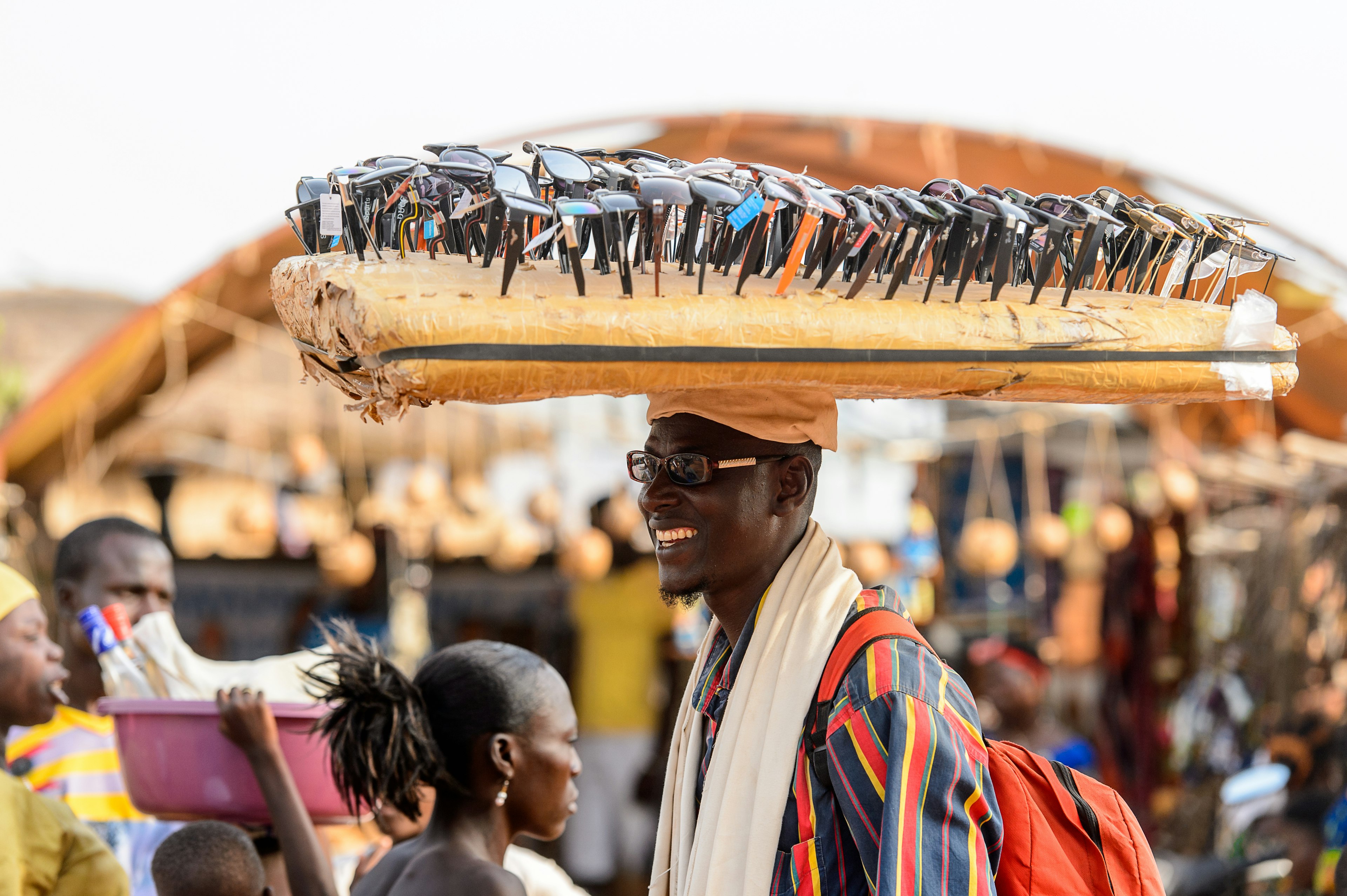 A Beninese man carries a lot of sunglasses on his head for sale at the local market.