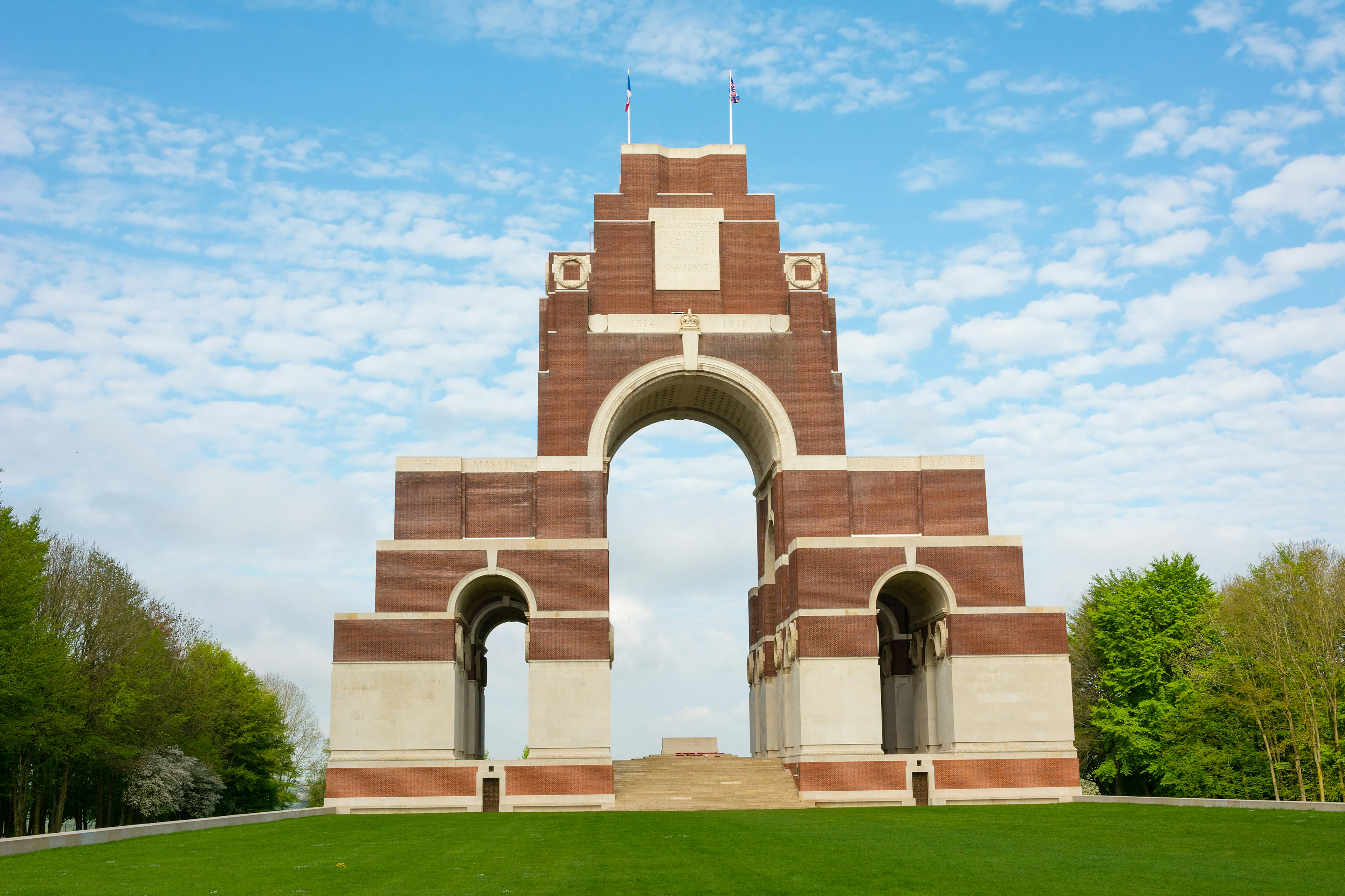 Thiepval Memorial in France; a memorial and burial site to some of those who died during the Battle of the Somme in the First World War. The monument is a large arched structure, while the surrounding laws are filled with poppies and small crosses acting as tombstones.