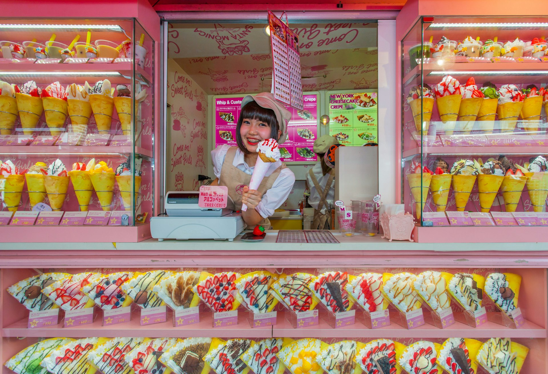 Young woman selling ice creams and crepes from a bright pink stall