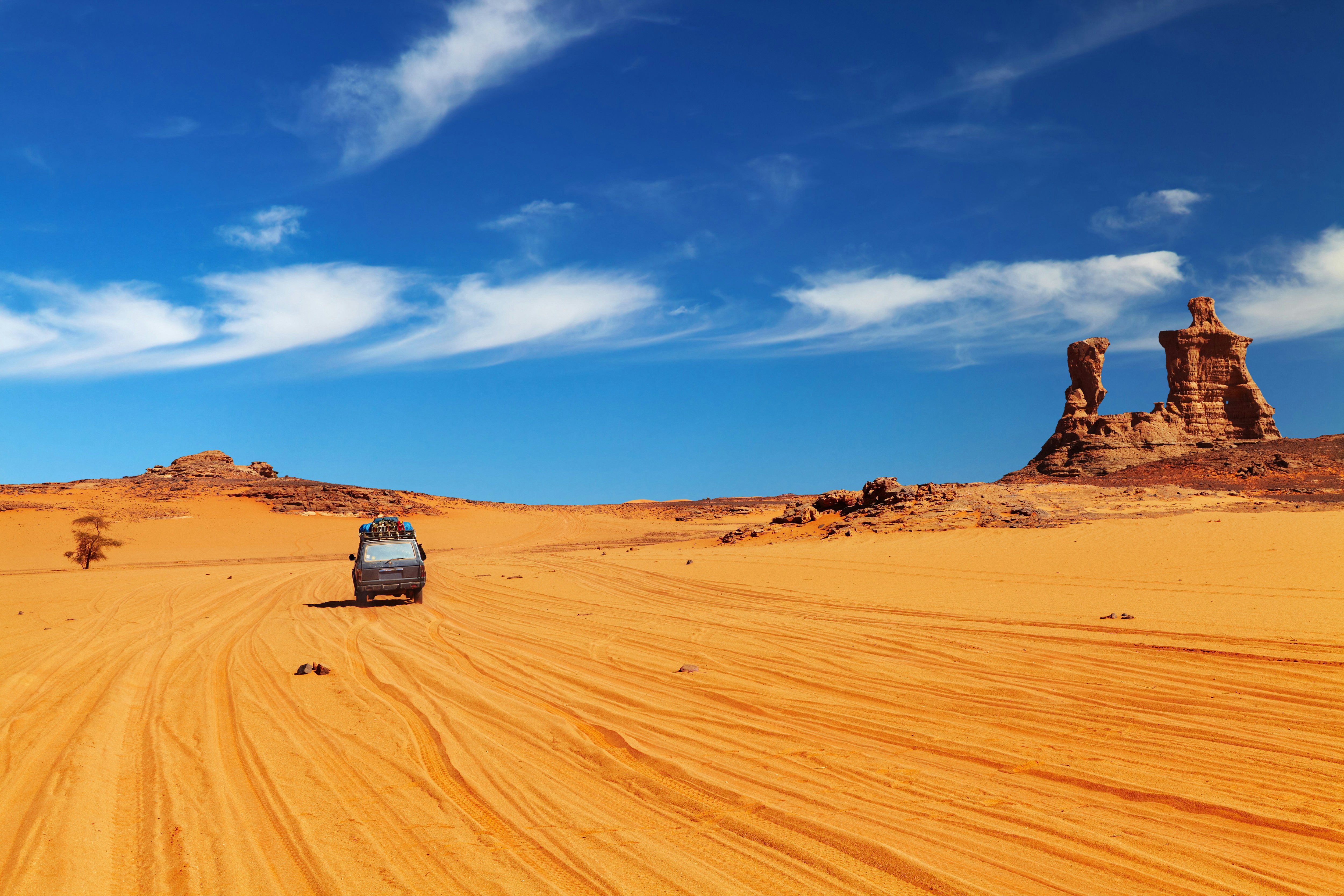 A vehicle drives on reddish sand with nothing but a rock formation on the horizon.