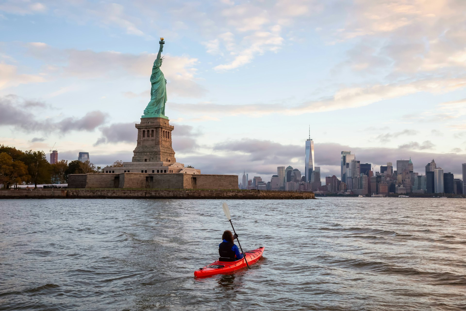 A red kayak in the water in front of the Statue of Liberty