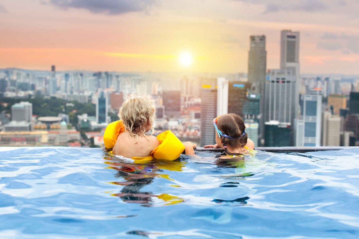 Children in a rooftop swimming pool looking at the Singapore skyline
