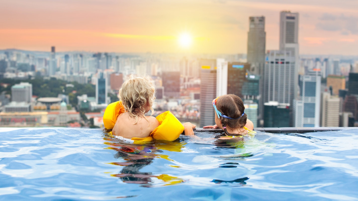 Children in a rooftop swimming pool looking at the Singapore skyline